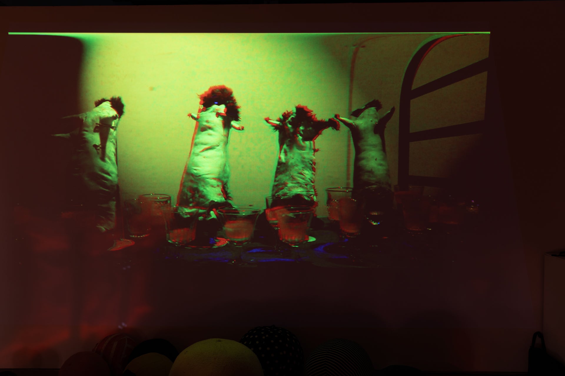 /A%20looped%20video%20of%20rabbit%20skins%20standing%20upright%20and%20wine%20glasses%20full%20of%20pepto%20bismol%20being%20pushed%20down%20a%20hallway%20on%20a%20work%20cart.