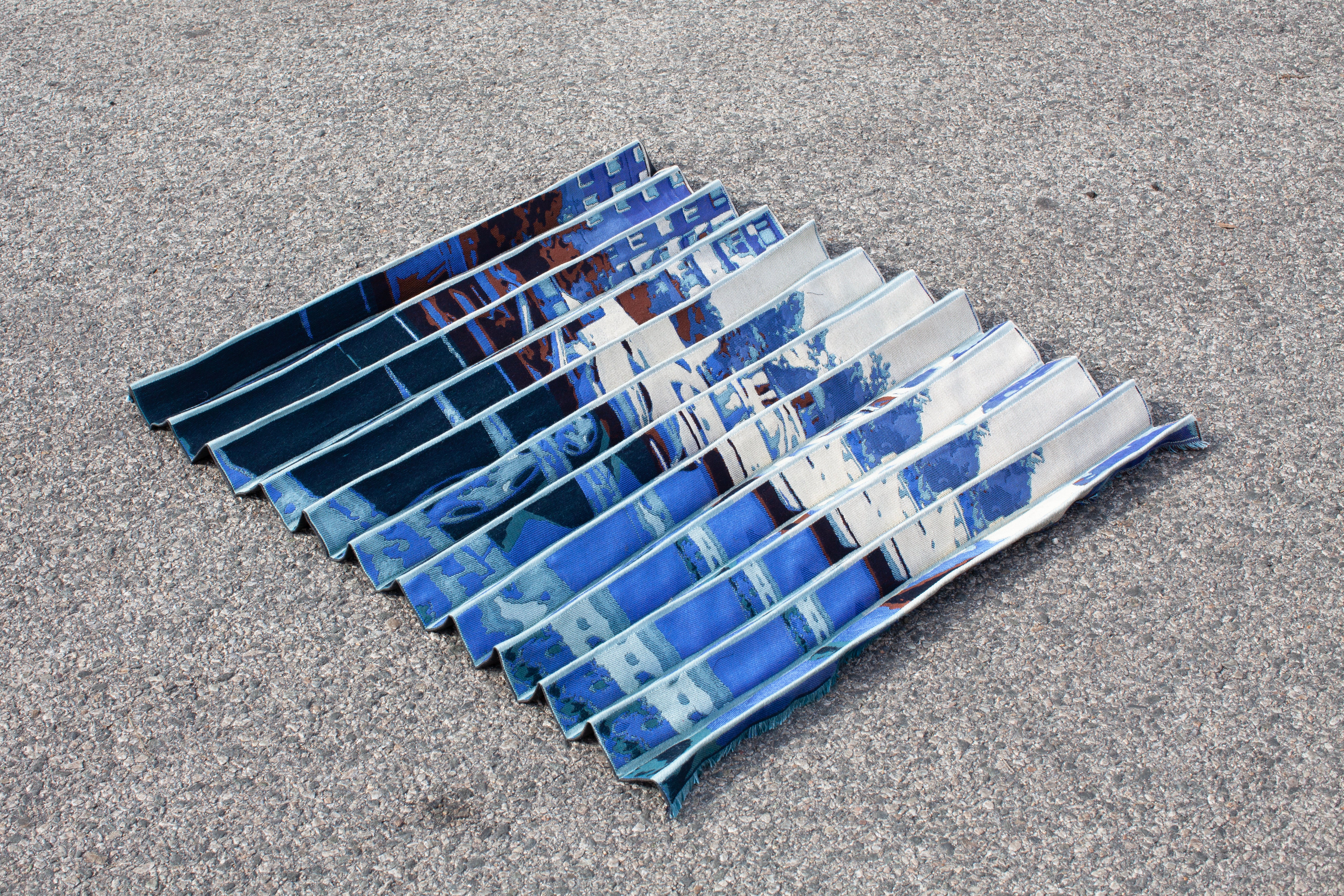 /Pleated%20woven%20textile%20depicting%20a%20glitched%20image%20of%20a%20street%20in%20a%20monochromatic%20blue%20color%20palette.