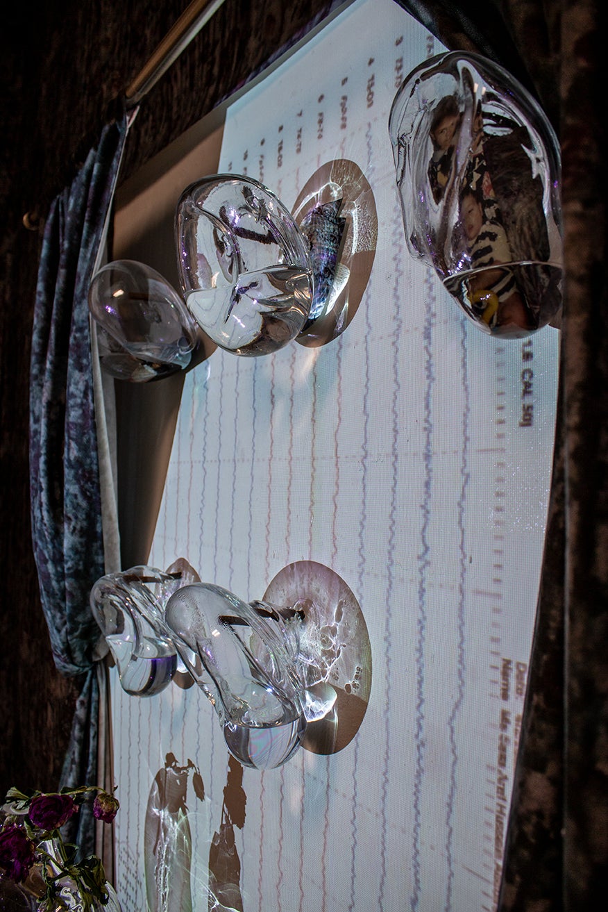 /Close-up%20detail%20of%20an%20intriguing%20installation.%20Glass%20orbs%20capture%20the%20impression%20of%20limbs%20from%20a%20casted%20body%2C%20delicately%20holding%20liquid%20and%20childhood%20photographs%20within%20them.%20