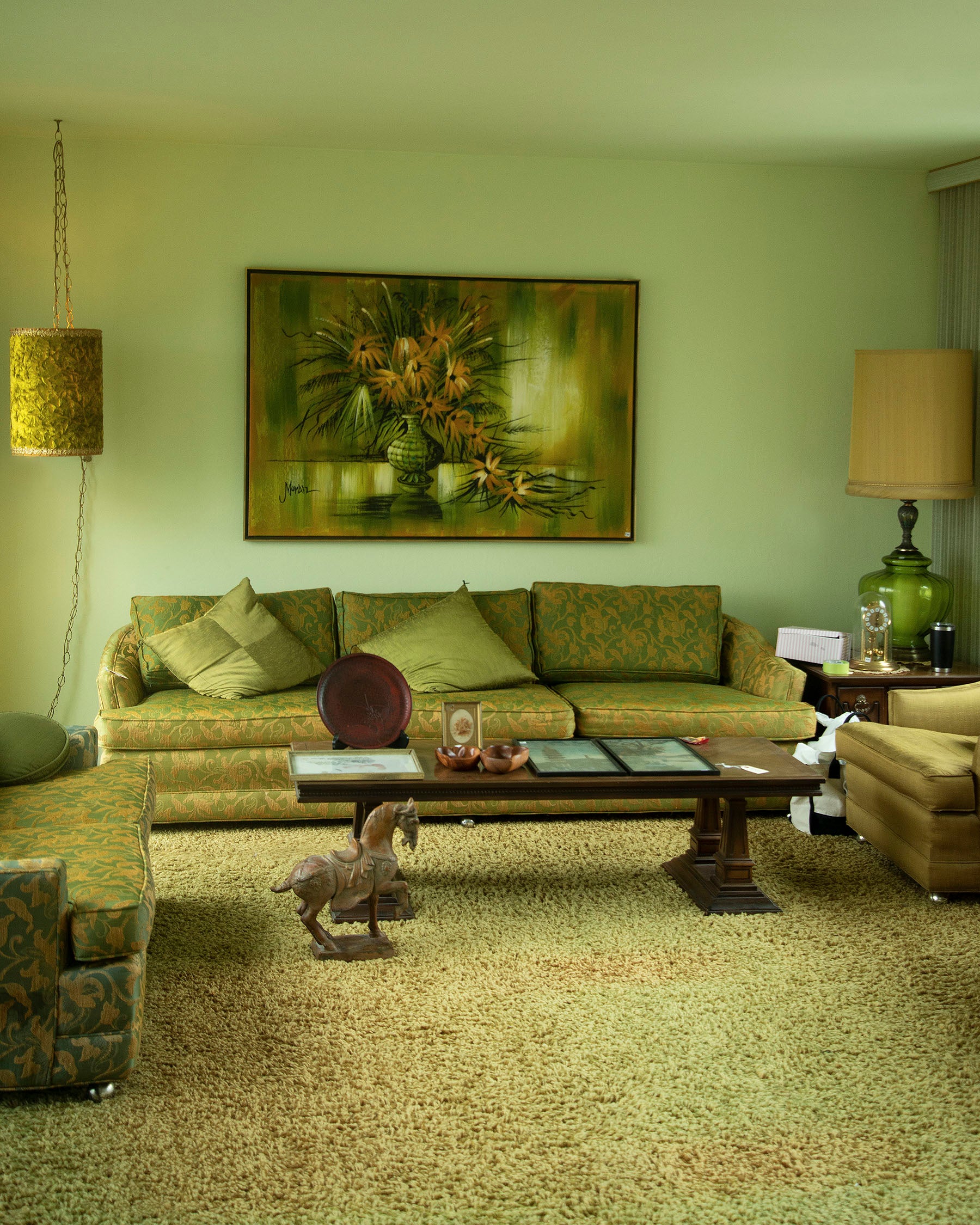 /An%20monochromatic%20%28olive%20green%29%20interior%20space%20of%20a%20mid-century%20modern%20living%20room%20paired%20with%20matching%20furniture.%20On%20the%20floor%20is%20a%20sculpture%20of%20a%20horse%20figurine%20and%20a%20coffee%20table.%20