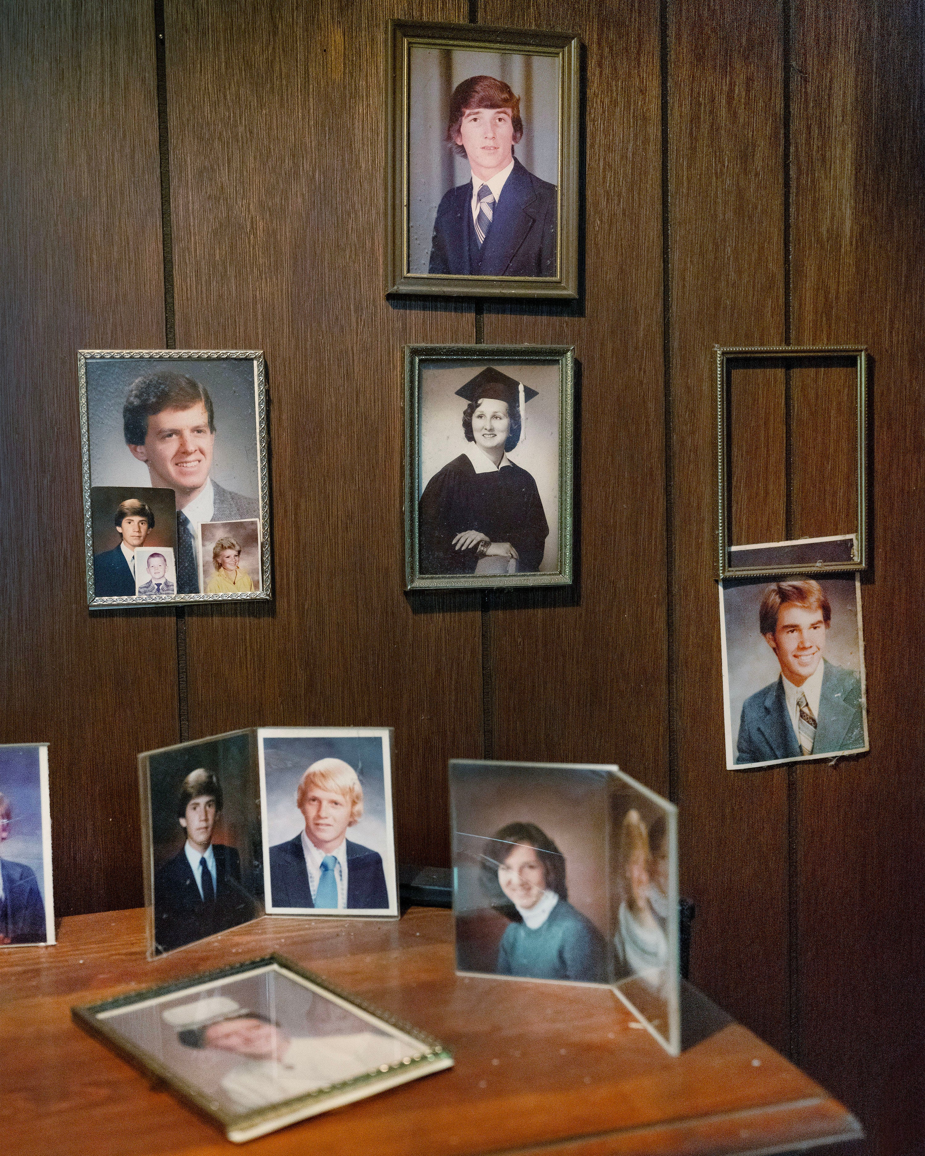 /Framed%20photographs%20mounted%20on%20a%20wood-paneled%20wall%20of%20men%20and%20women%20in%20various%20portraits.%20A%20sidetable%20below%20features%20additional%20photographs.
