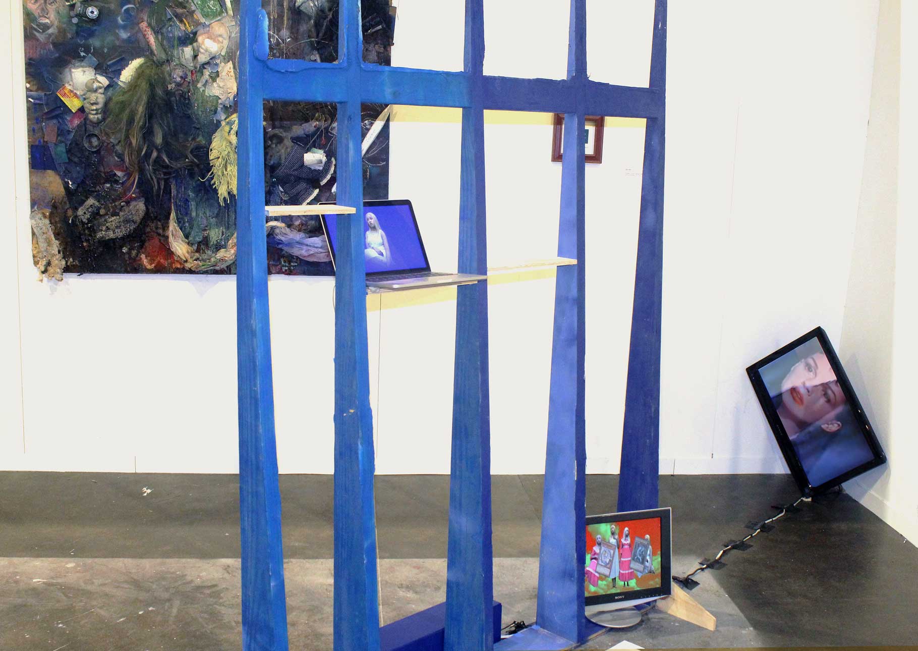 A large blue gate-like structure with shelves stands center. Untitled (Blue Portrait) is on the left shelf, DARKMAGICIANGIRL on the right. P.A.I.N. is on a screen in the right corner. STREETHTRASH and Highest Heaven, Deepest Hell are on the back wall.