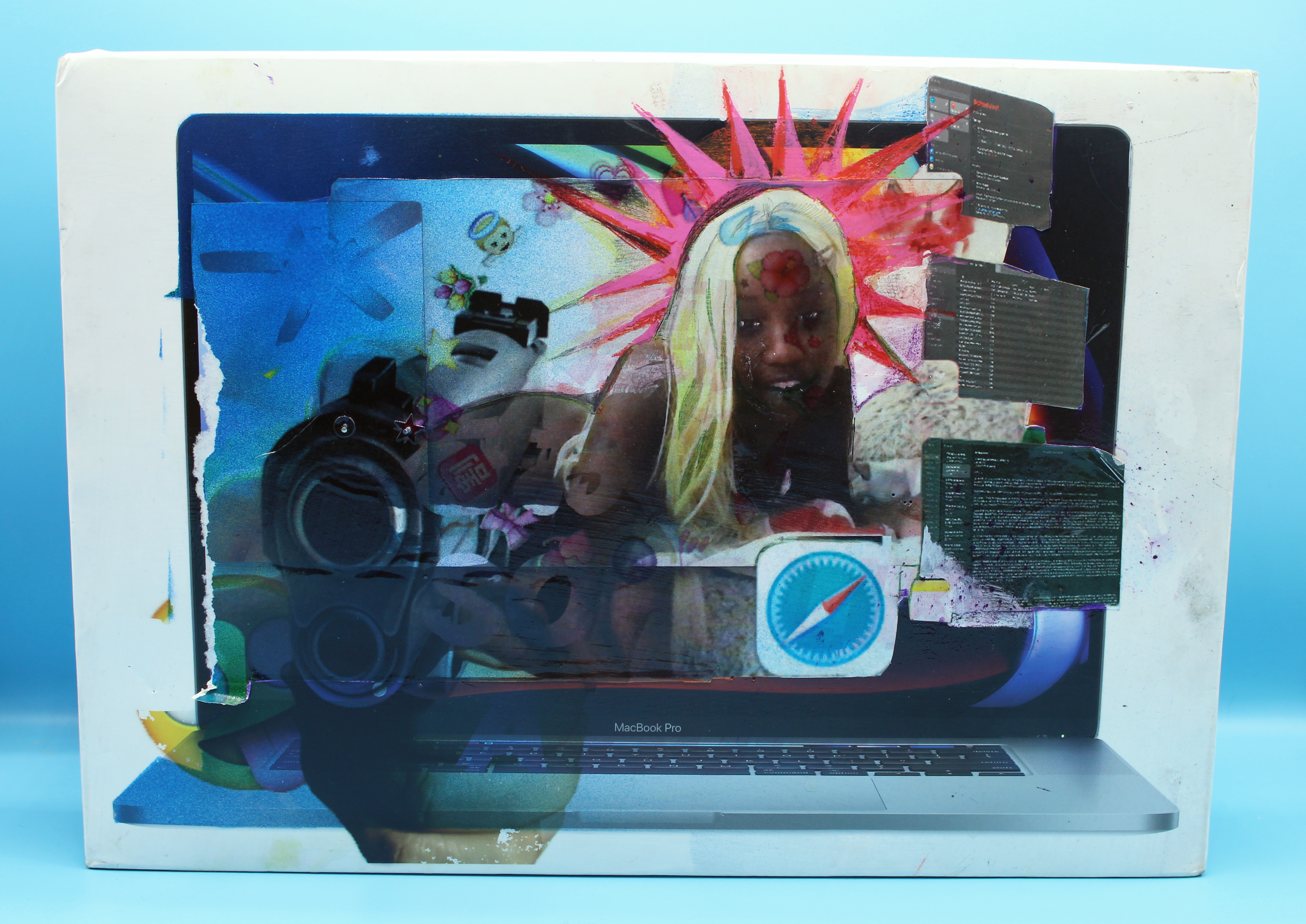 A Macbook Pro 2019 box in a periwinkle light-box. An image of the artist is collaged in the center of the box and surrounded by emojis. There is a hand holding a gun toward the viewer UV printed on the lower-left of the box.