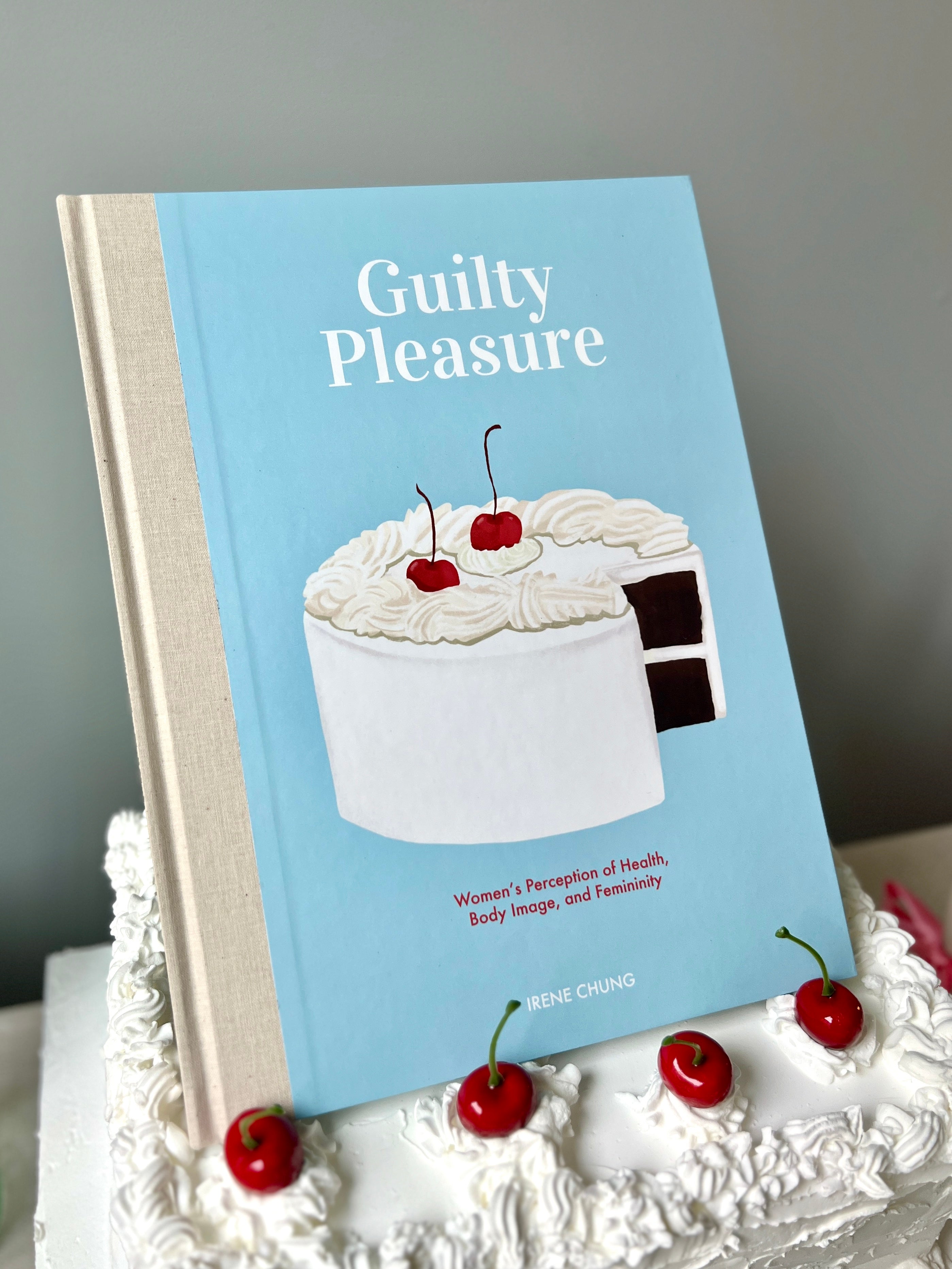 an illustrated book, titled Guilty Pleasure, sitting on a cake with cherries on top 