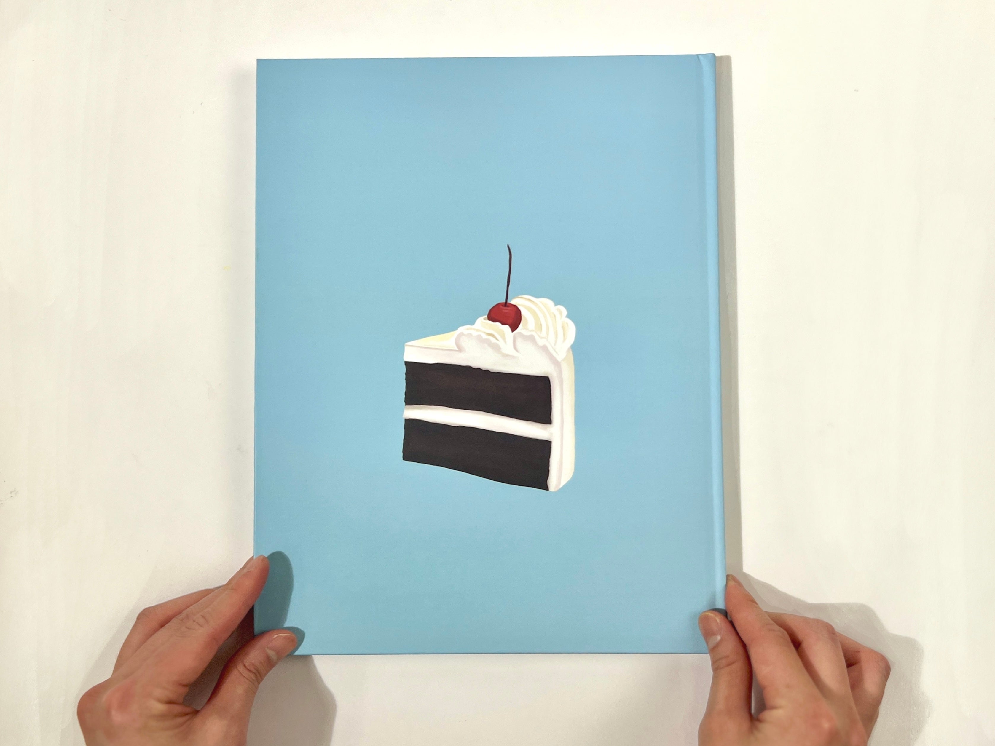 /A%20photograph%20of%20the%20book%20cover%2C%20which%20features%20a%20piece%20of%20creamy%20white%20cake%20with%20a%20cherry%20on%20top%2C%20sitting%20on%20a%20baby-blue%20background