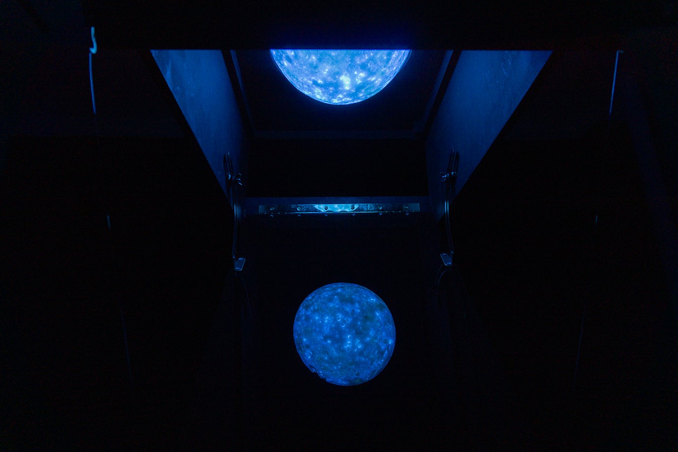 A fluorescent blue moon appears in a dark room, reflecting off an angled acrylic sheet, creating a captivating and ethereal visual effect.