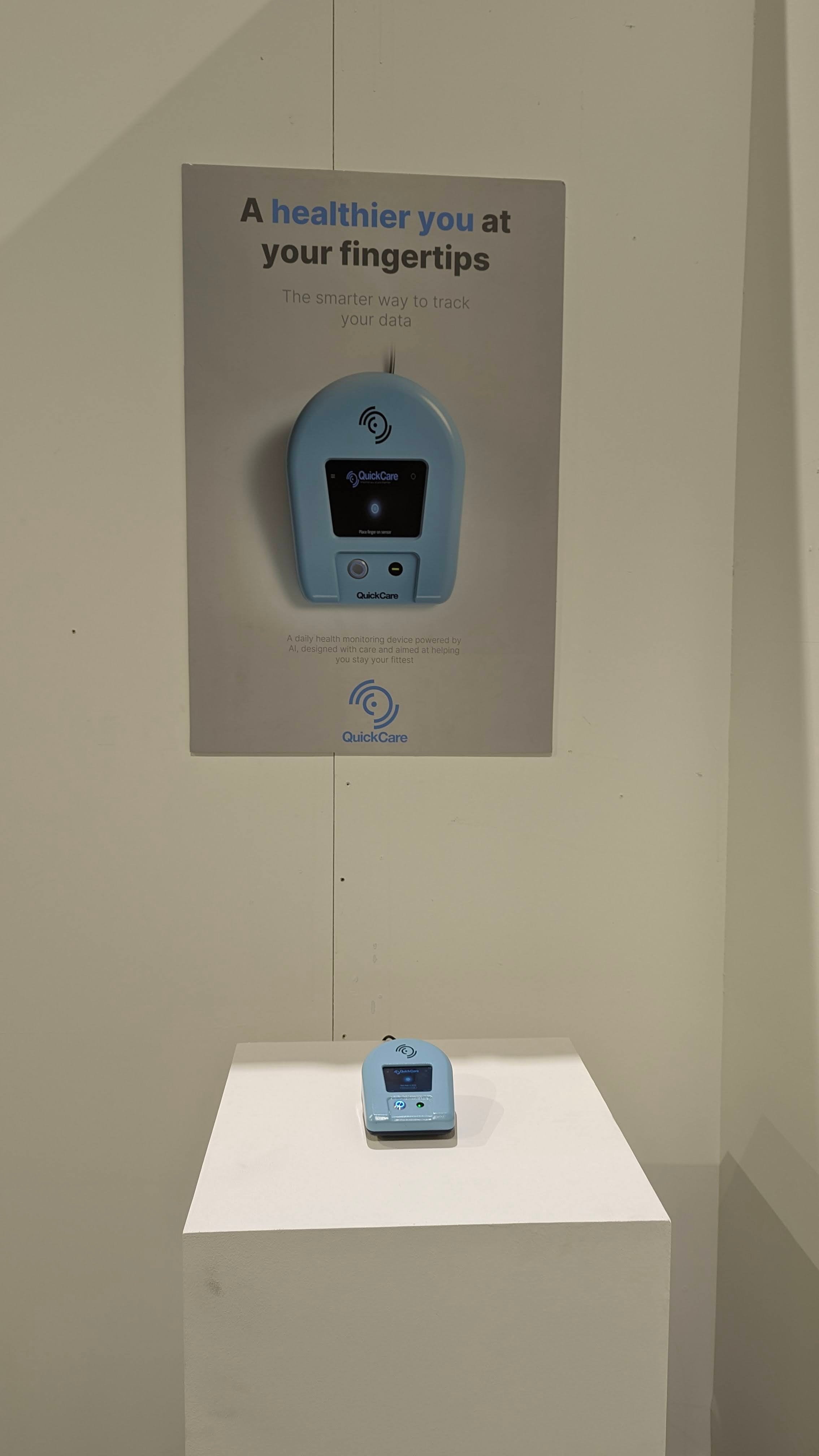 QuickCare product on pedestal placed in a corner between two promotional product posters. One poster has a QR that leads to an online product page.