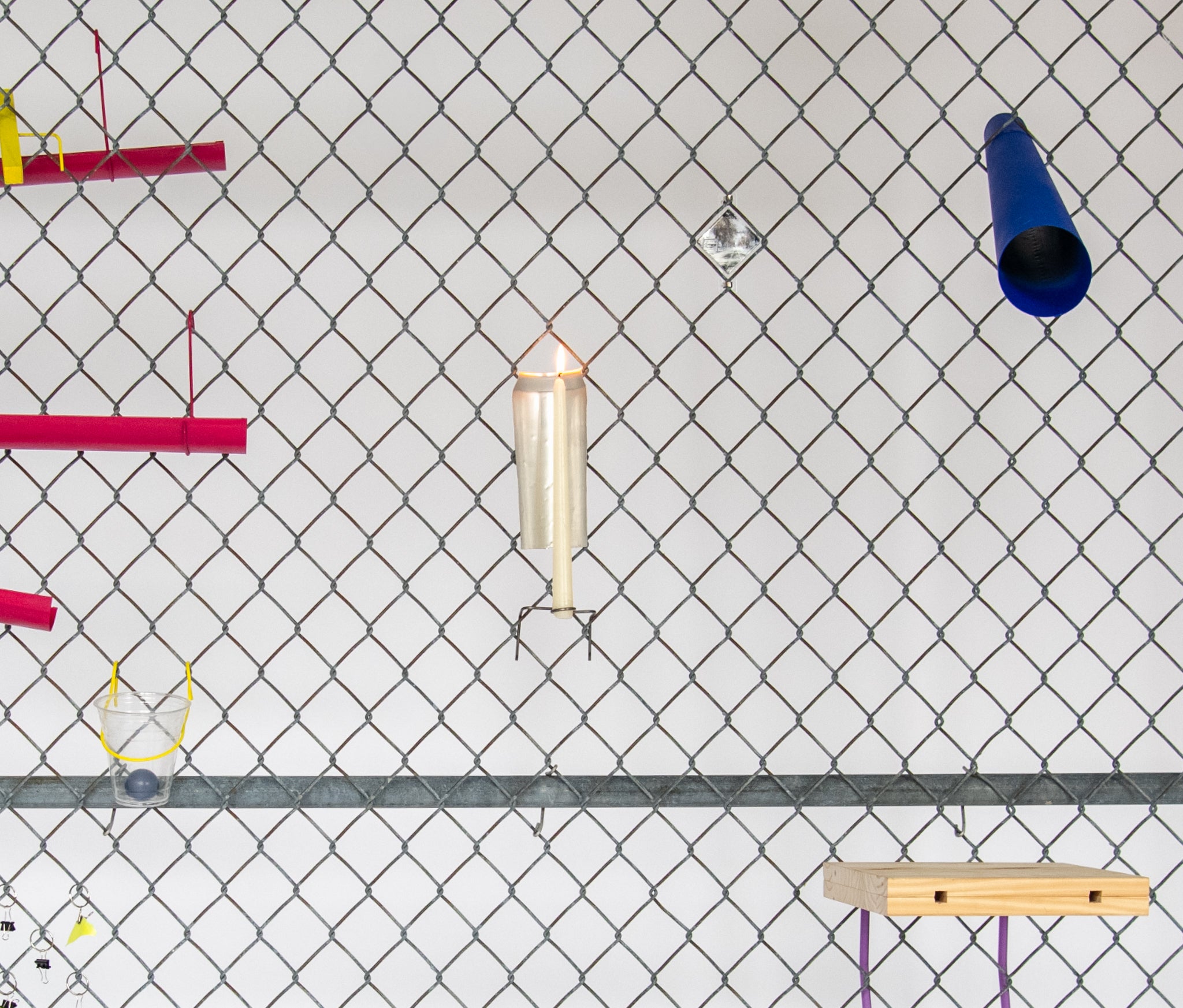 Close up of a chain link fence with various designed objects affixed to it, including a candle holder and a blue telescope.