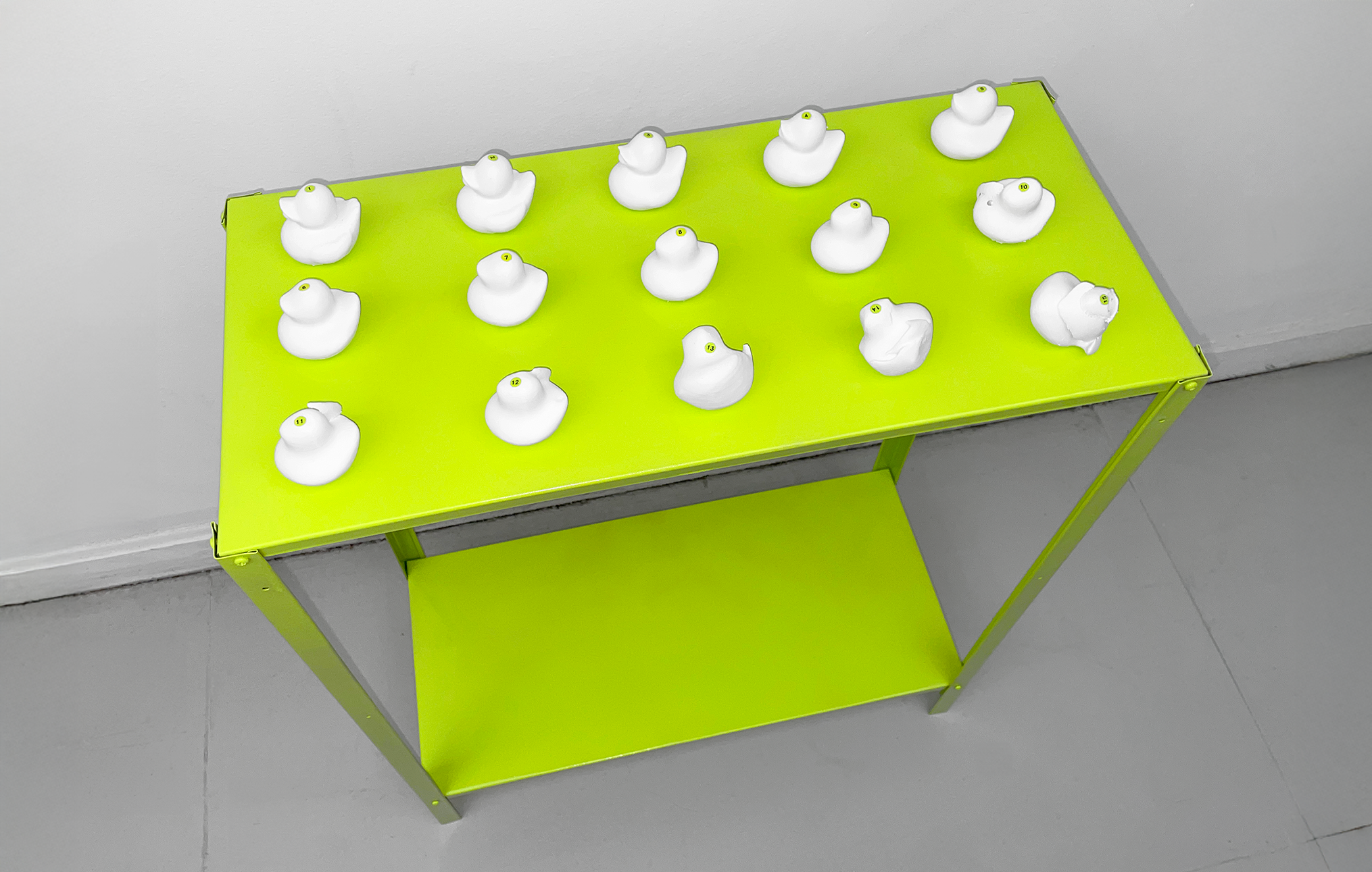 3D-printed white duck sculptures on a lime green shelf, each slightly distorted with numbered stickers indicating sequence.