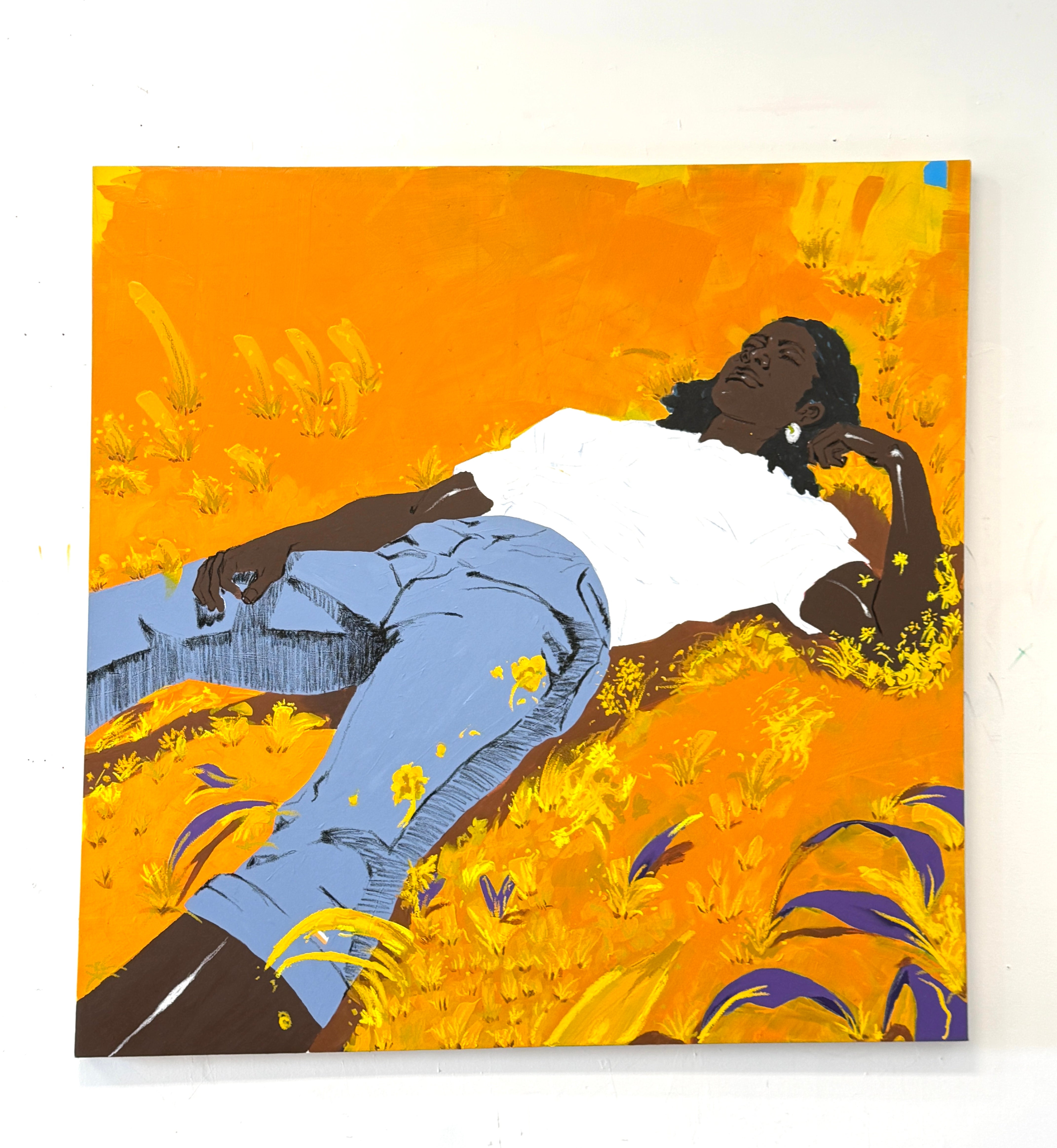 A Black woman lying in a golden field, surrounded by yellow and purple foliage, wearing a white t-shirt and light blue jeans.