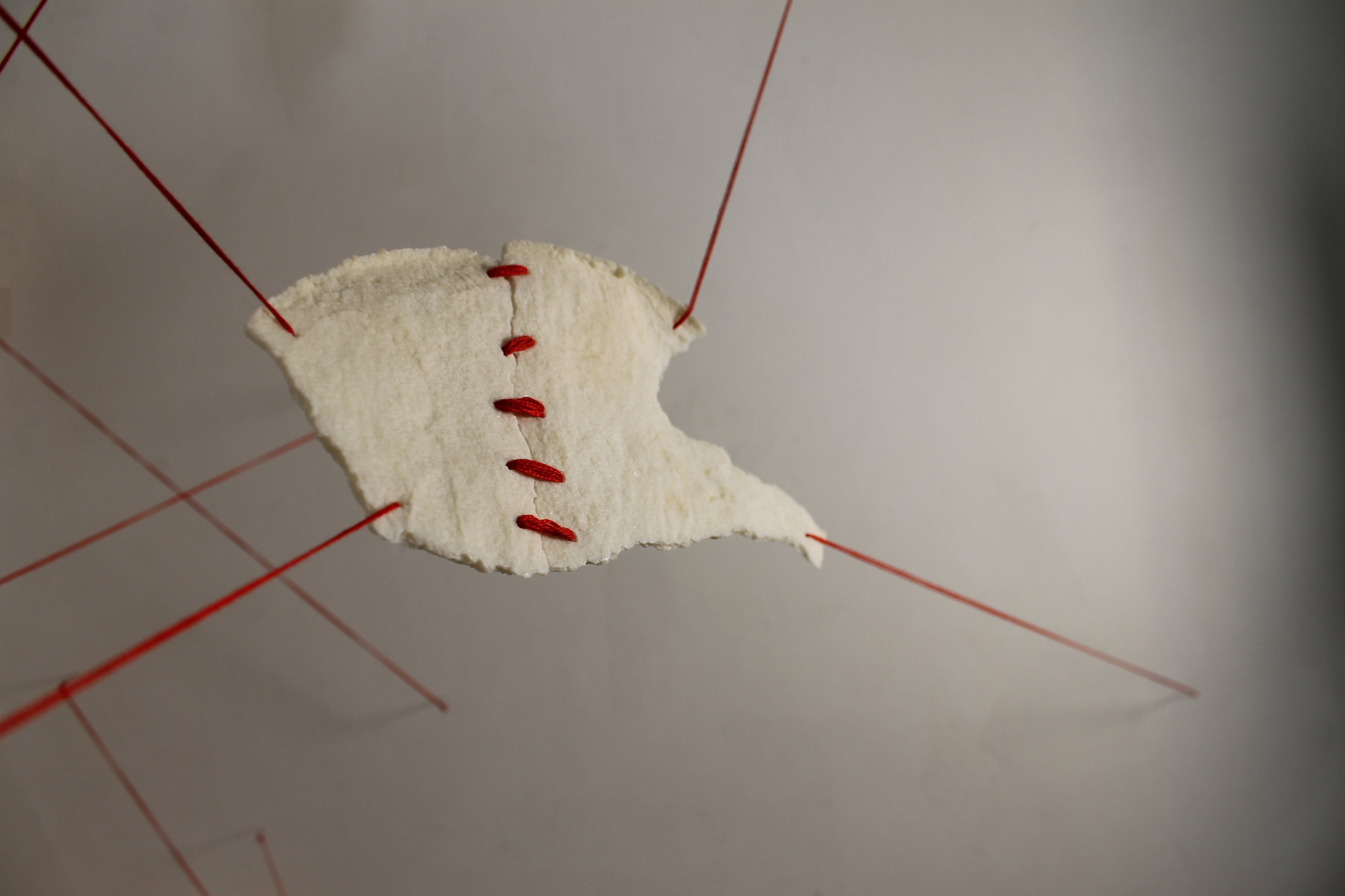 Fragmented pieces of Nablus soap stitched at the center with red thread, suspended with threads pulling from each corner.