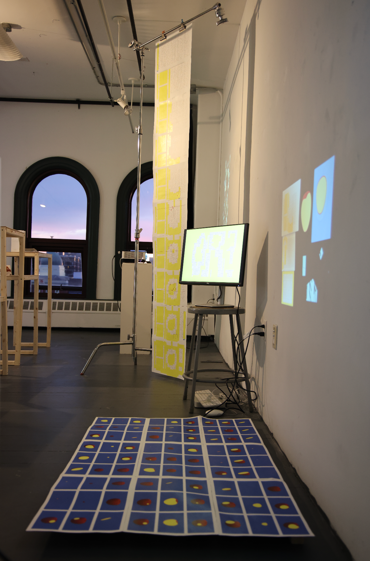 Art installation with hanging scroll, digital screen, projection, and blue grid of circular prints on the floor