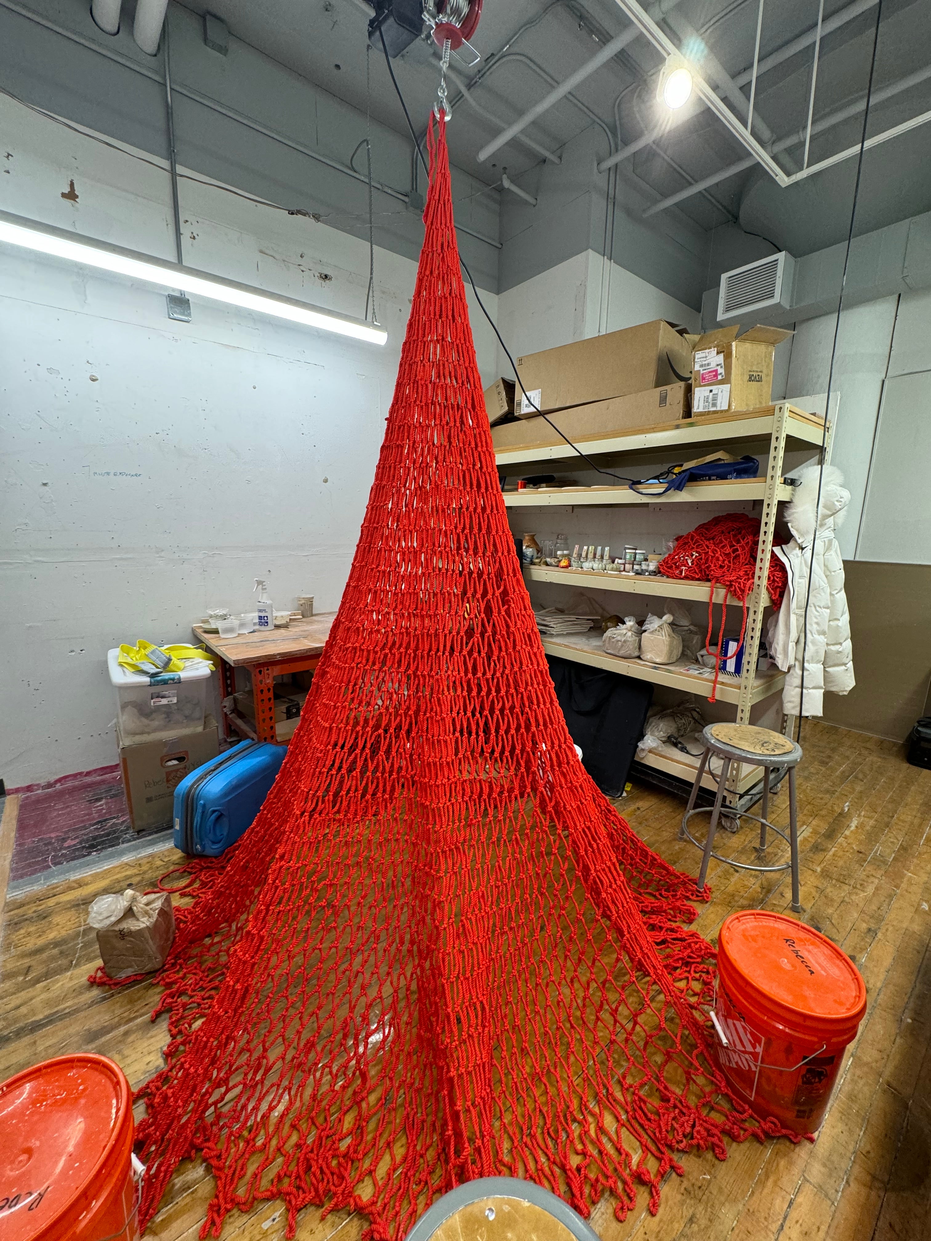 Red net hanged with ceramic objects dangled from a hoist. Hoist perform motion of let net spread on floor and pull it back up