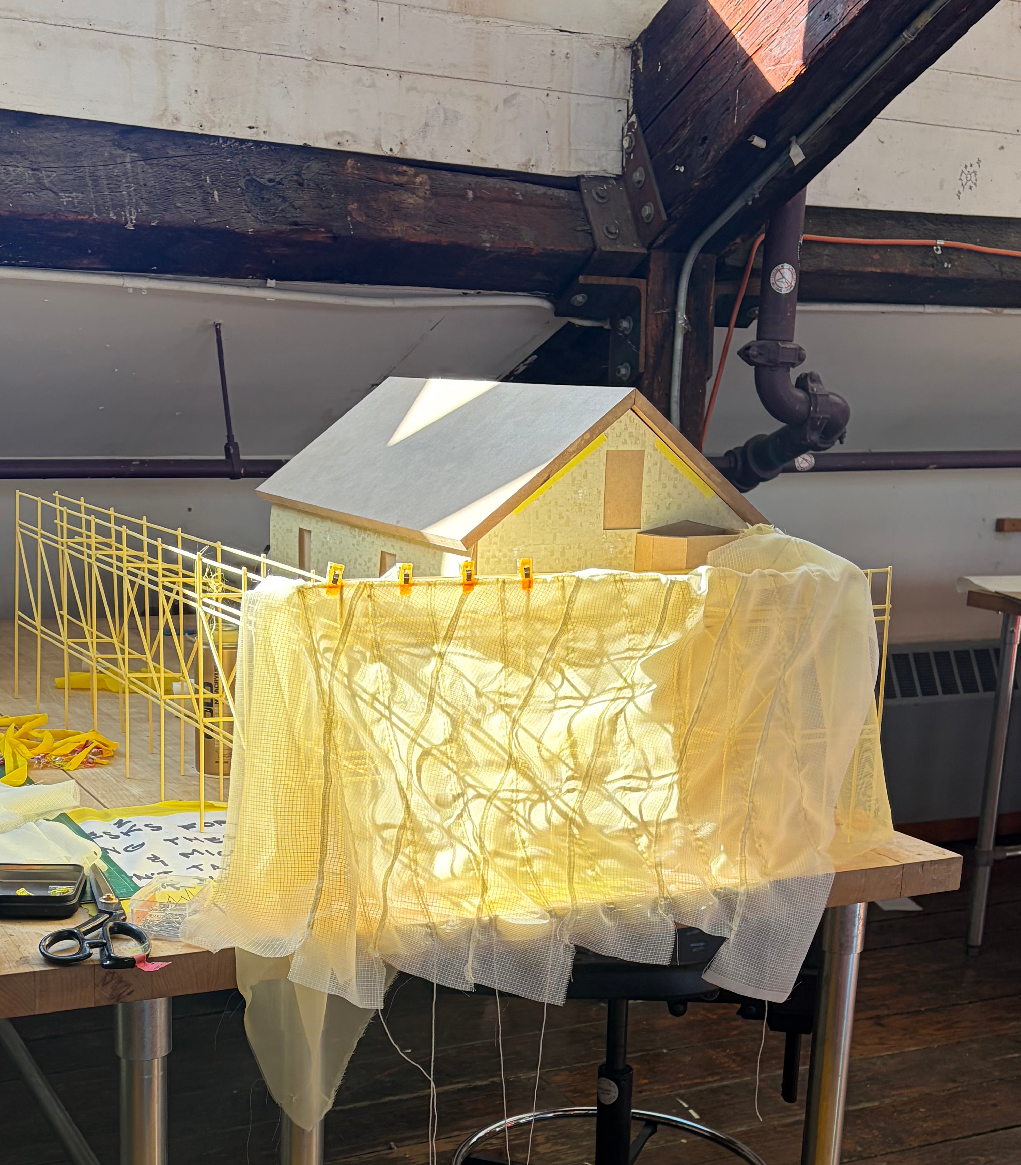 Layers of yellow fabric sewn and draped over scaffolding with house model behind. photo taken on studio desk