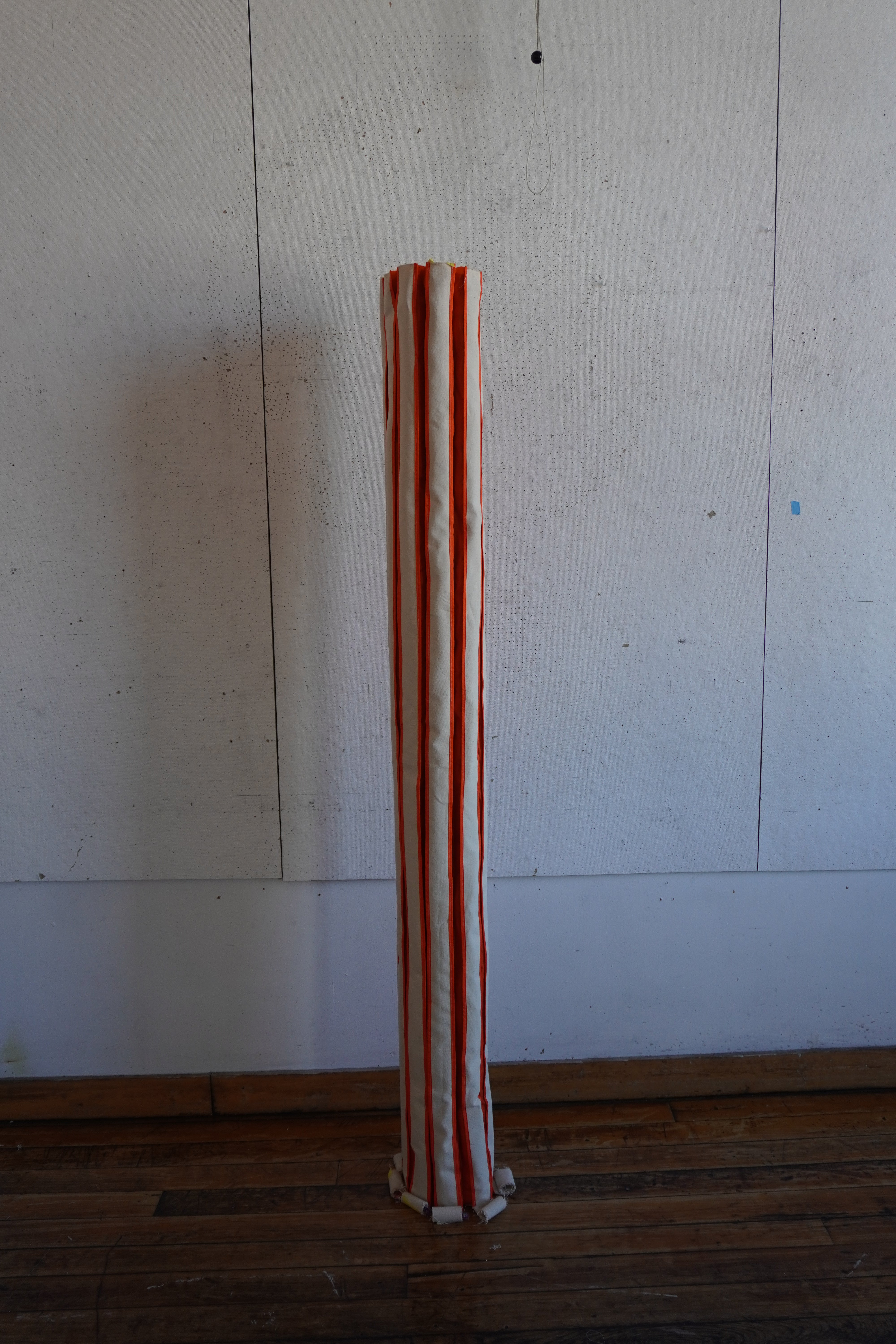 skinny fabric collumn standing on its own with orange stripes running from the floor to the top.
