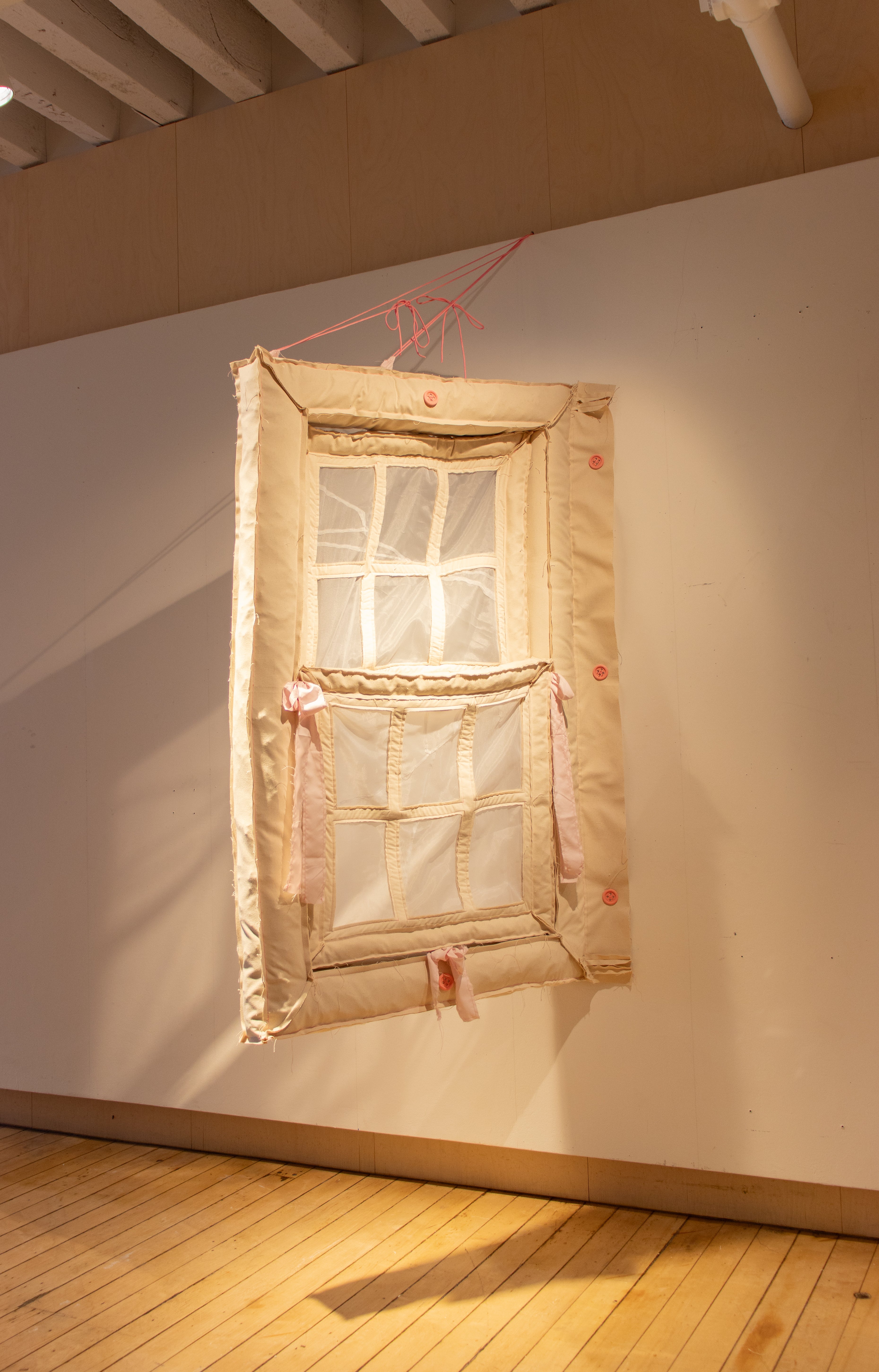 Hanging window made of off-white canvas fabric. 3 large pink buttons attach it to the wall.