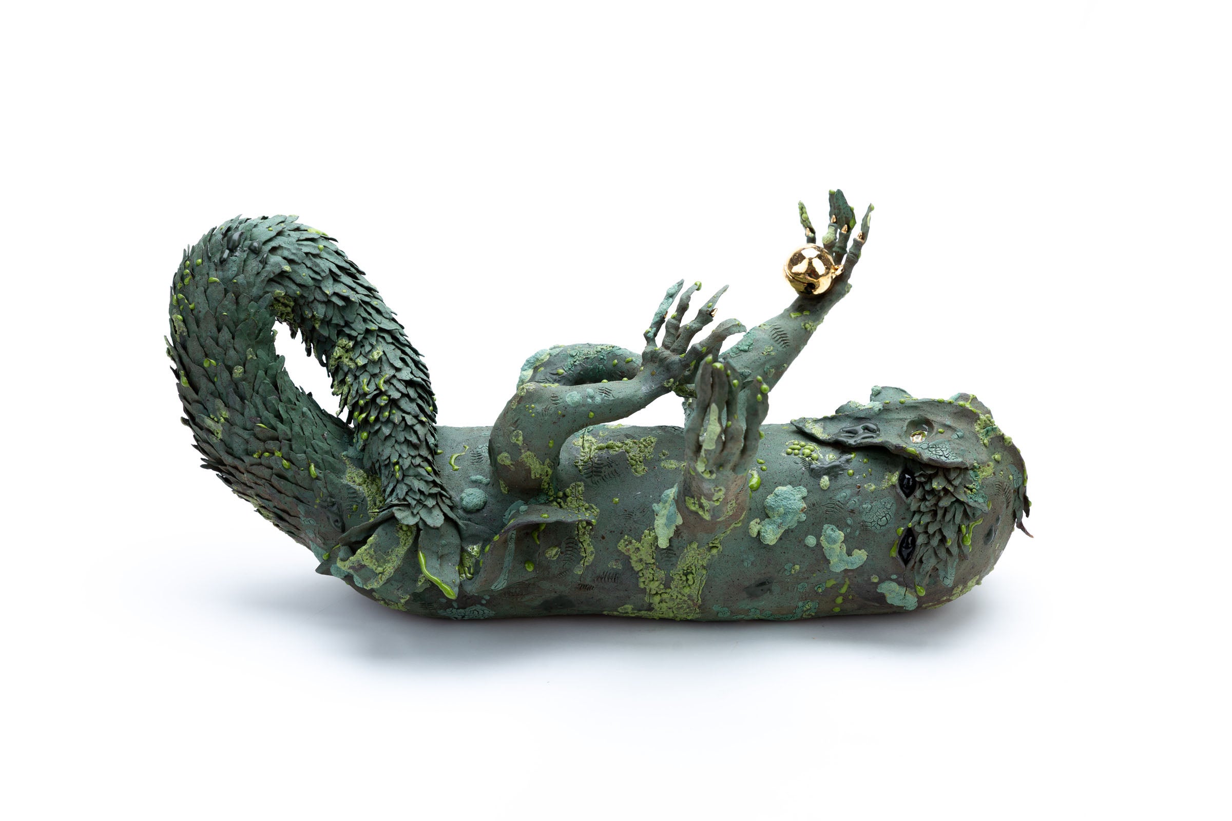 A green four legged creature lying on its back and reaching up to the sky. It has a twisting leafy tail, and is covered in mossy texturing. It holds a golden bell in one hand.