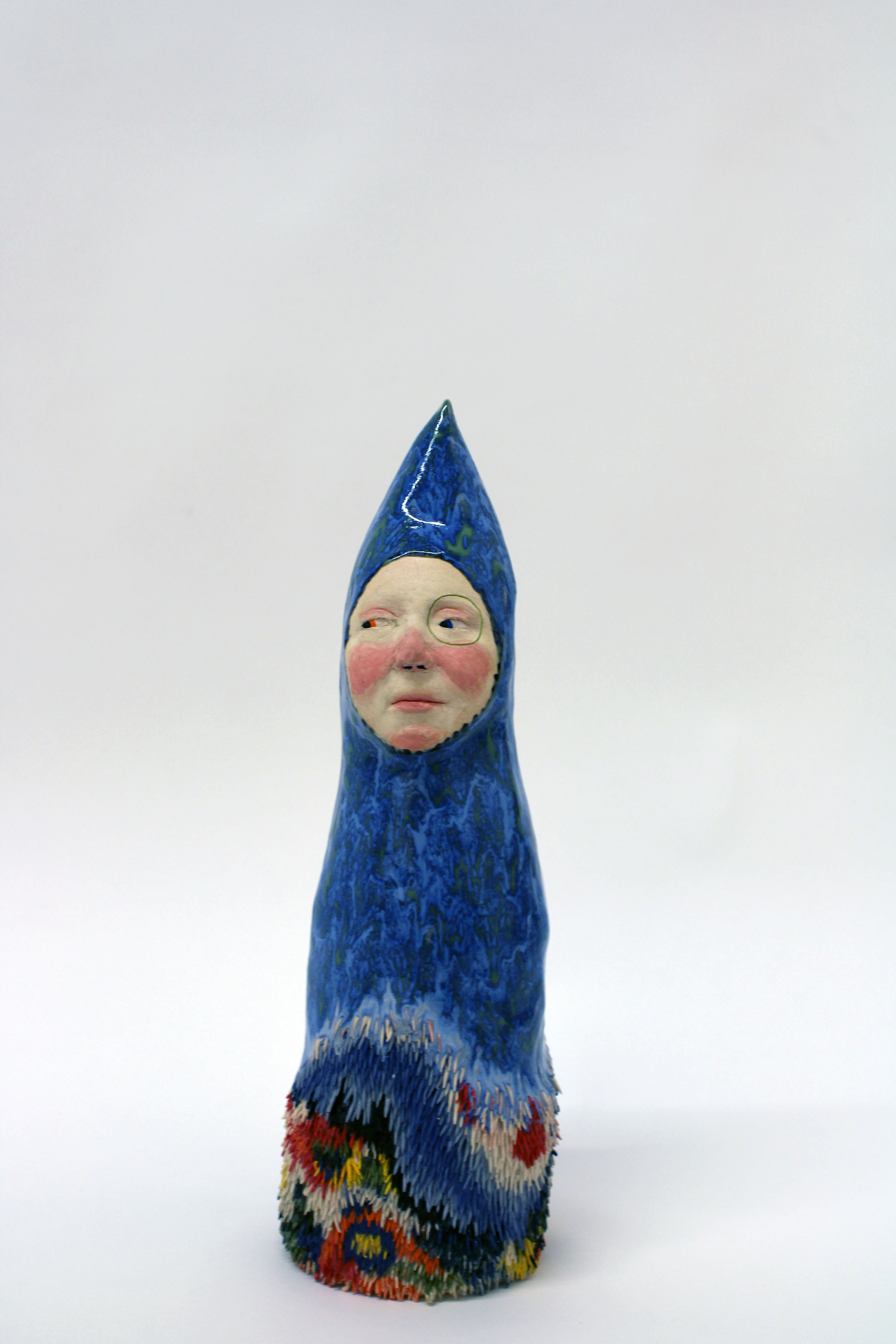 A blue and green small monolithic figure, with its face being a sort of flesh-colored window sticking out. There is some colorful fur at the bottom.