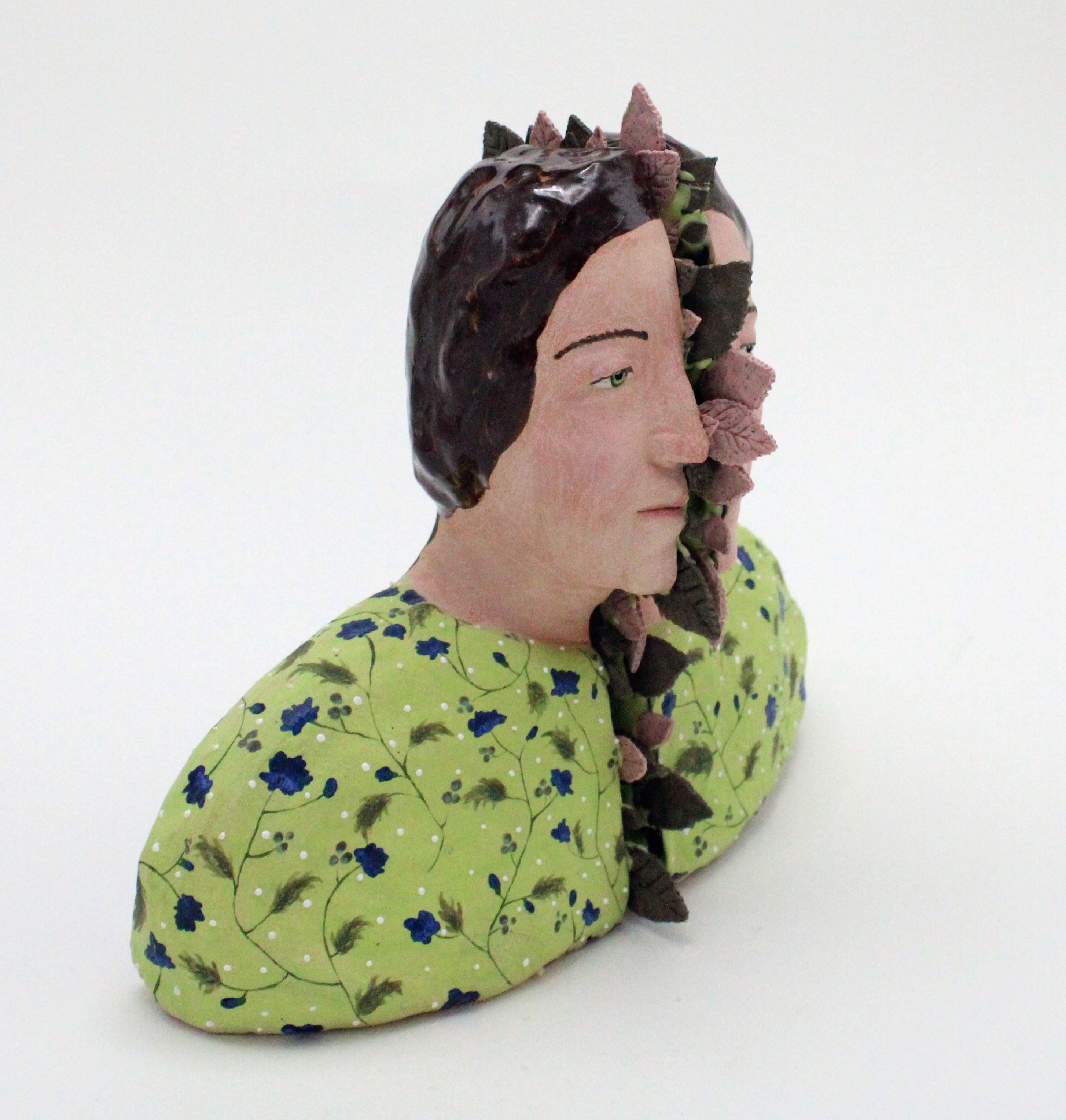 A bust of a woman split in half by green and pink leaves. She is wearing a green shirt with blue floral patterns