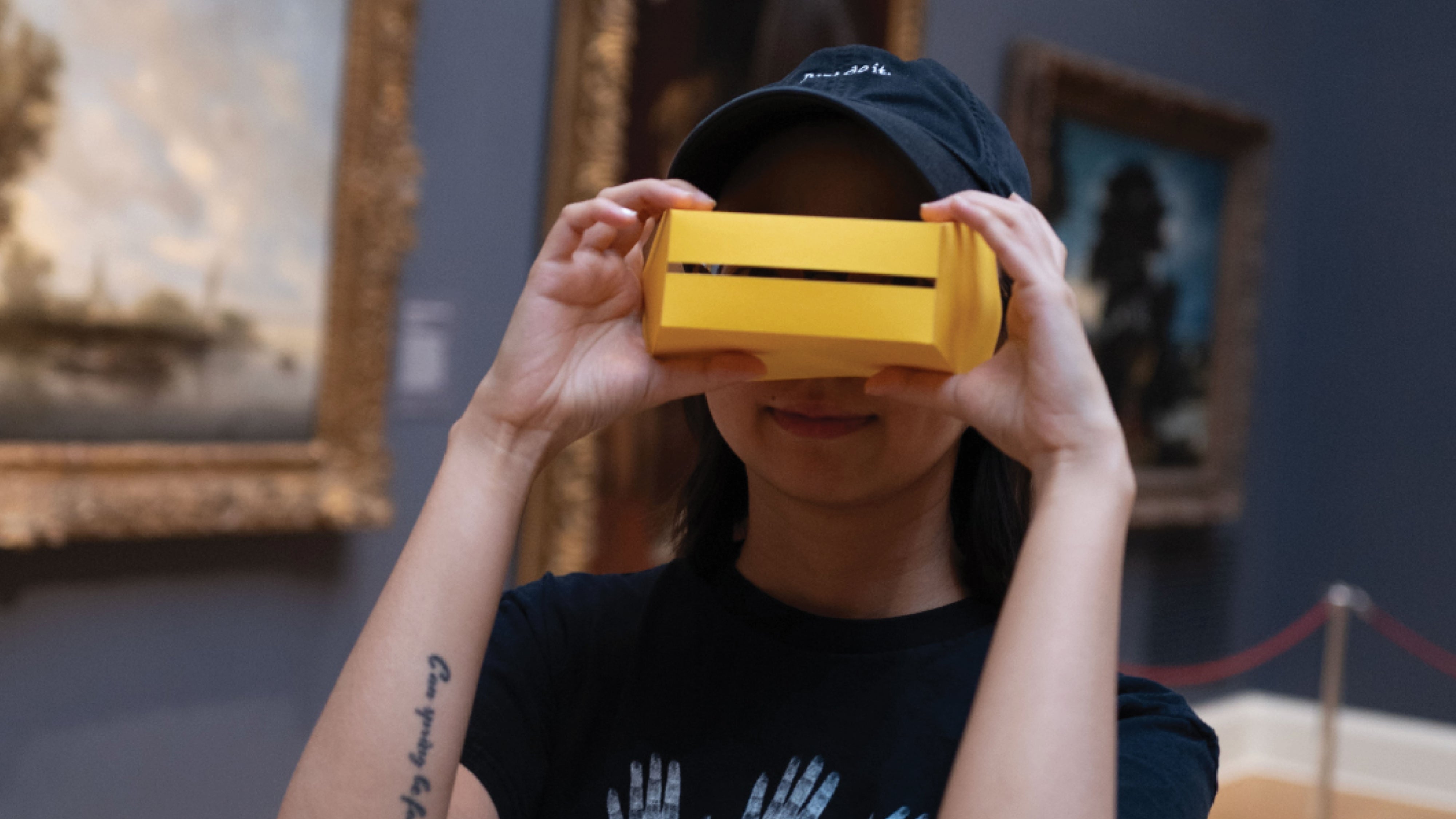 A person inside an art museum looking at the camera and wearing a yellow shape as glasses. 