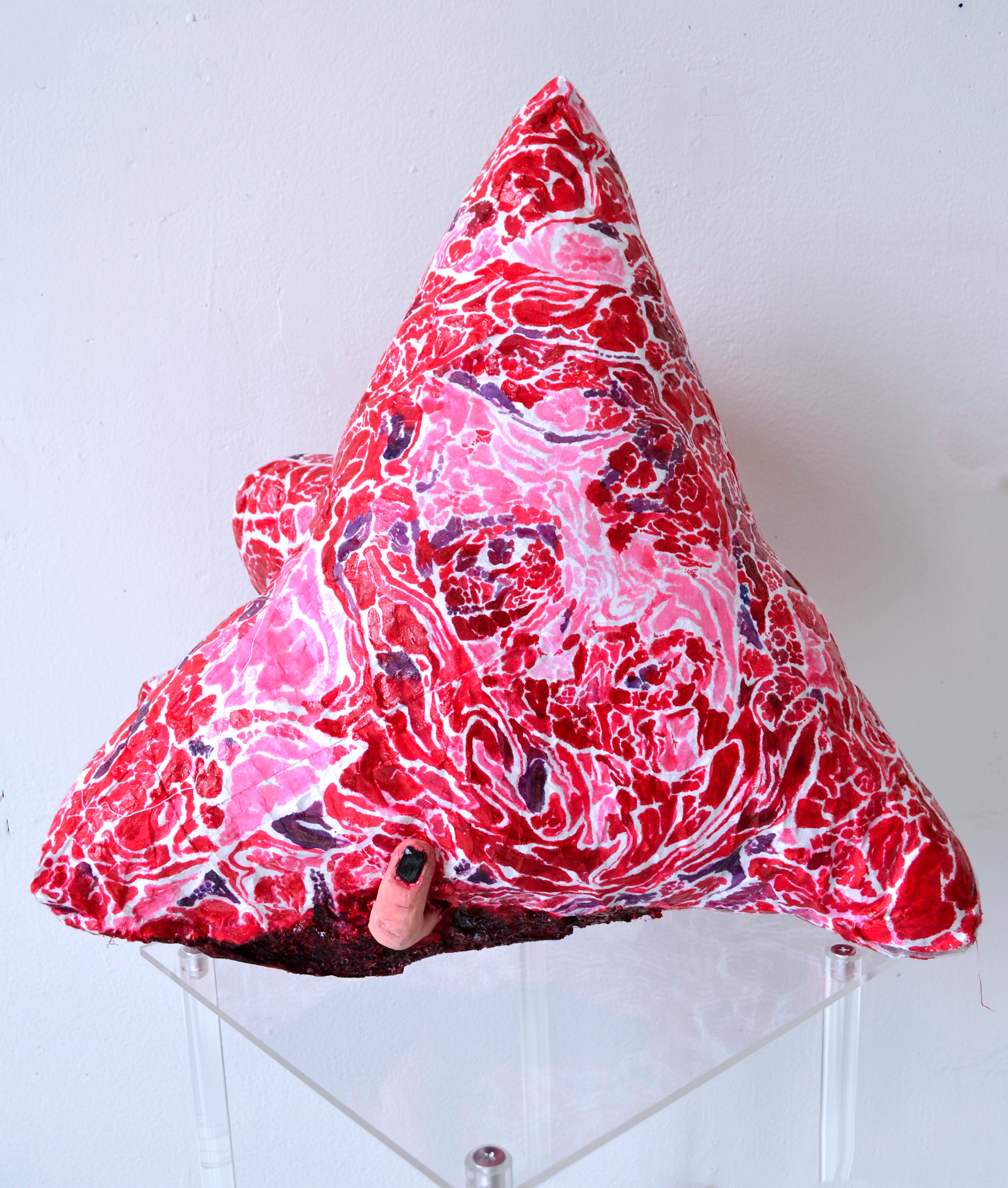 A triangular soft sculpture with a patterned painted surface mimicking a meat texture. 