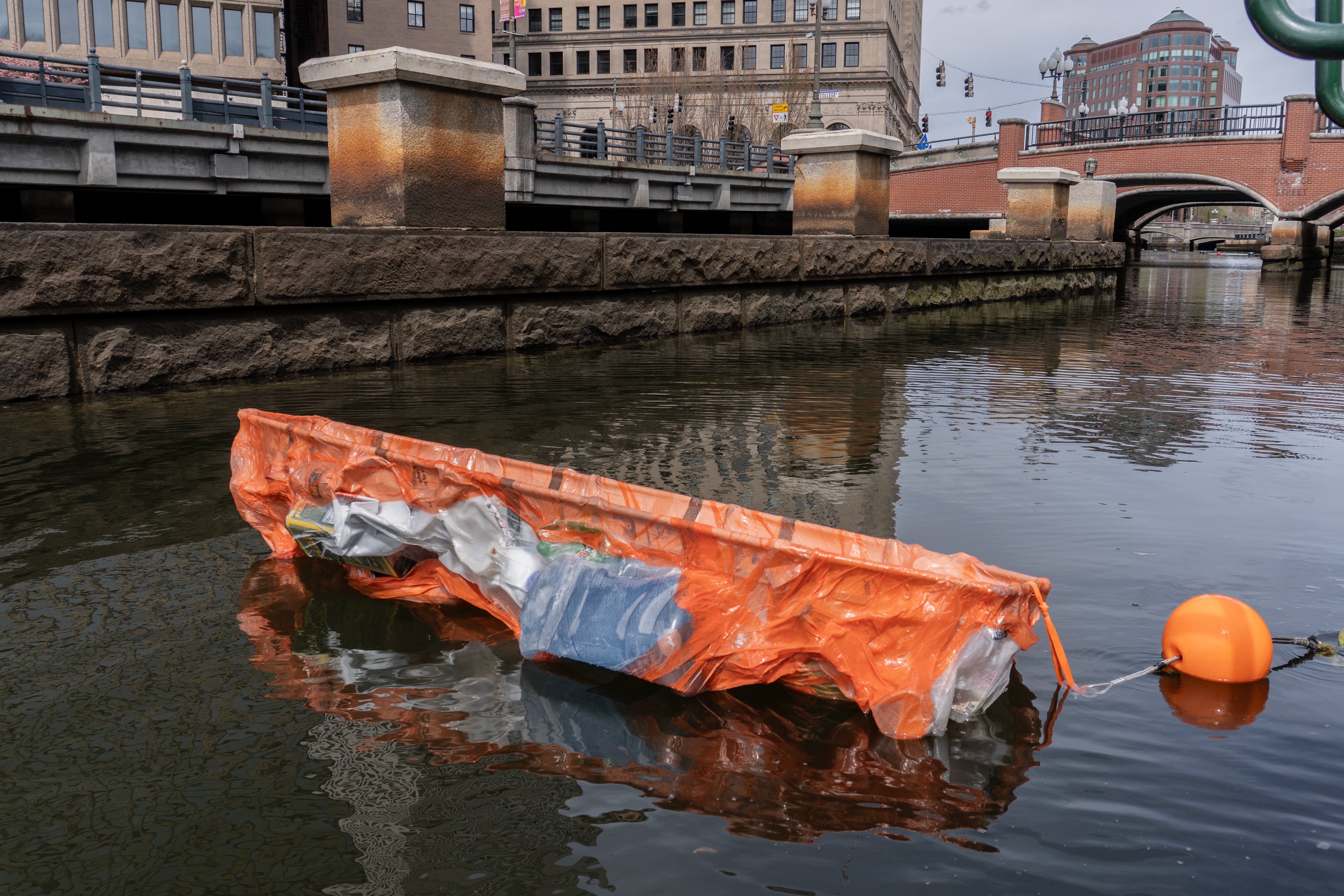 A bright orange stain in the middle of the river. Made from plastic bottles packed into orange plastic bags, vacuum-formed around a rescued bed into a compressed, airtight body. Inside, burned “mummies” made from thin black metal sheets, pressed into my  body.