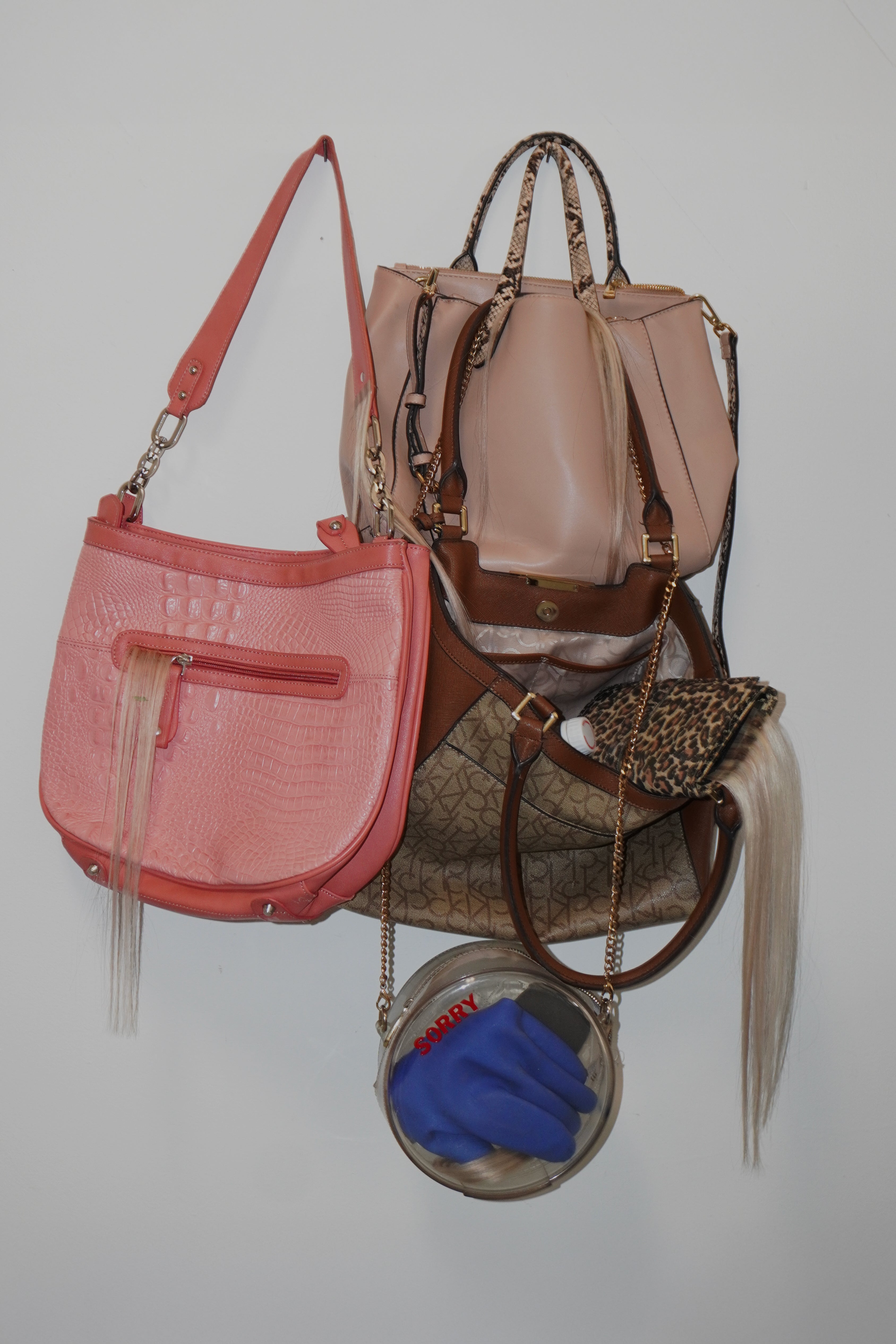 Stolen bags hang, hair coming out from the seams. Inside, a glove and a vinyl “sorry” sticker.