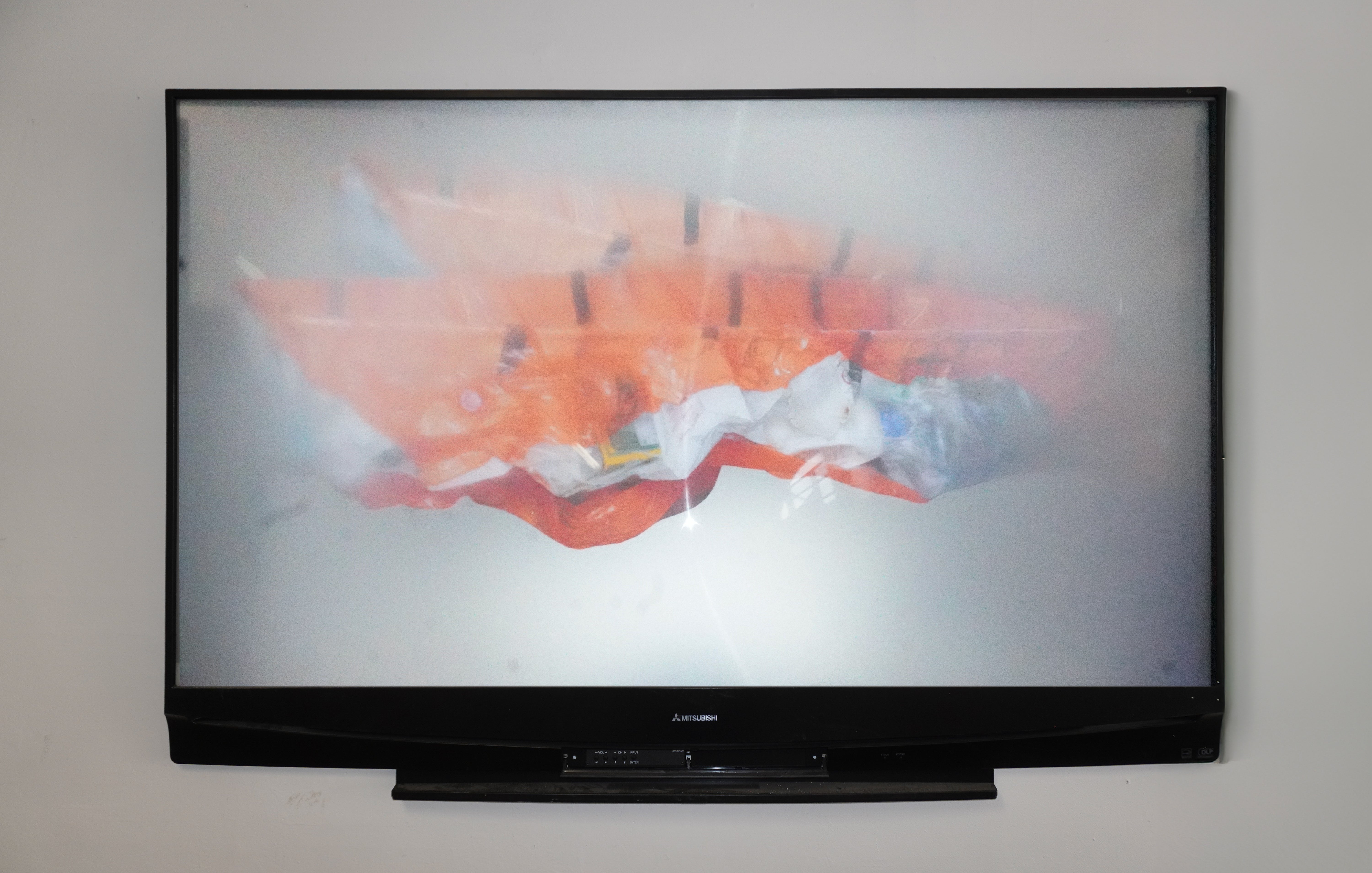 "A disassembled TV screen with a Fresnel lens. On the back, an archival paper print of the orange plastic boat sculpture, distorted through the lens. "