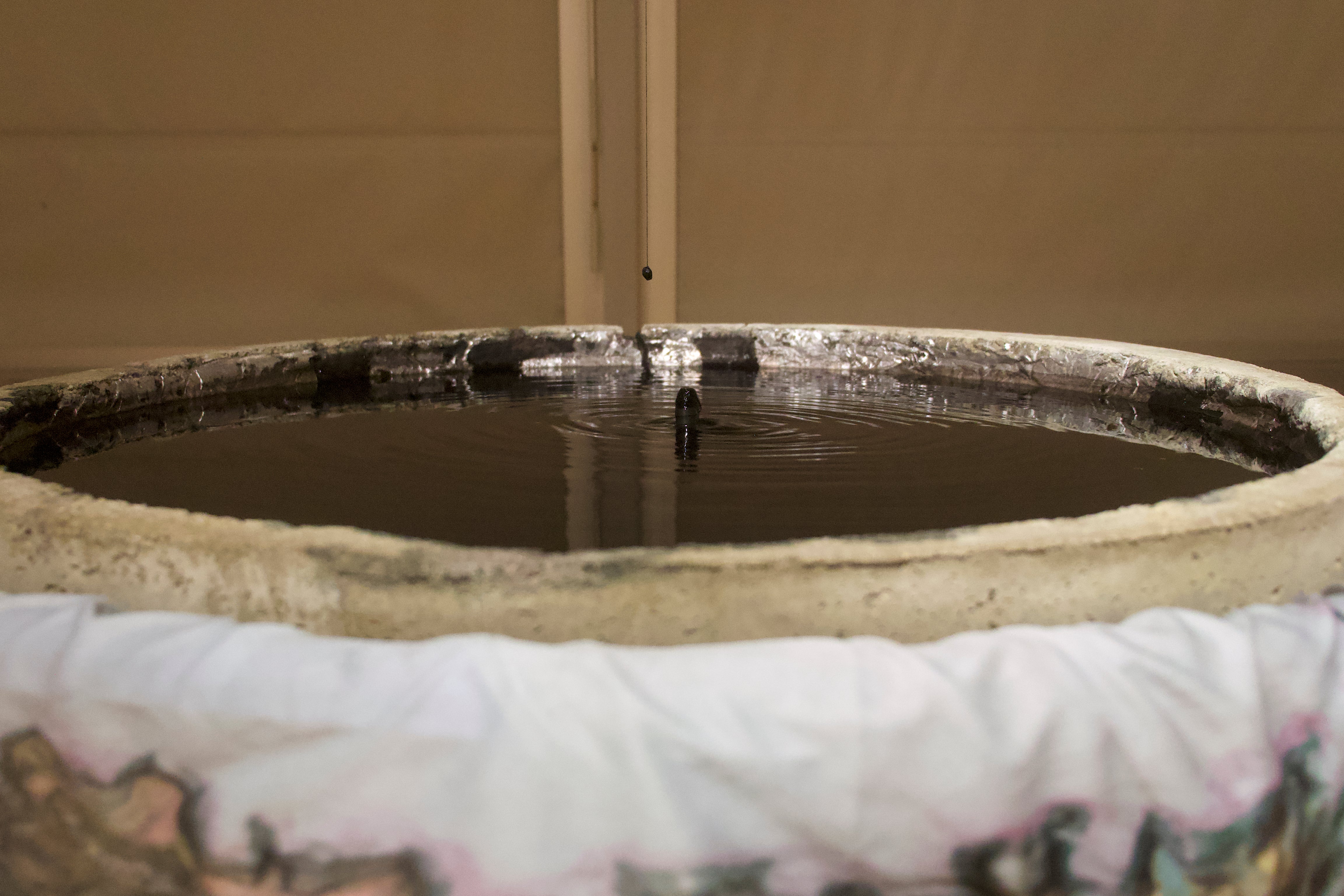 Close-up of dark rippling water in a concrete basin, with a small black bead suspended above the surface.