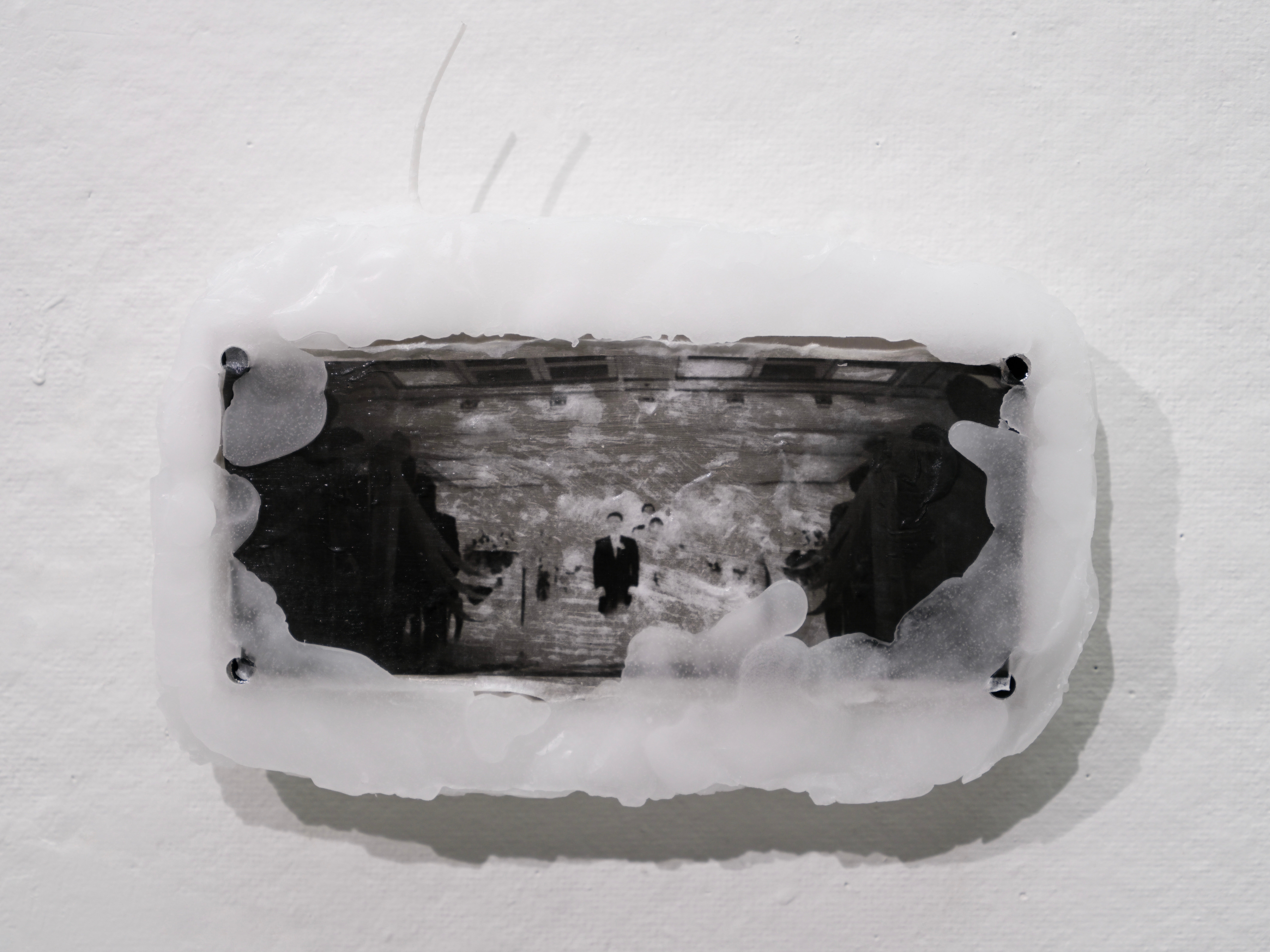 Close-up of a black-and-white family photograph partially covered in white paraffin and mounted on a wall.