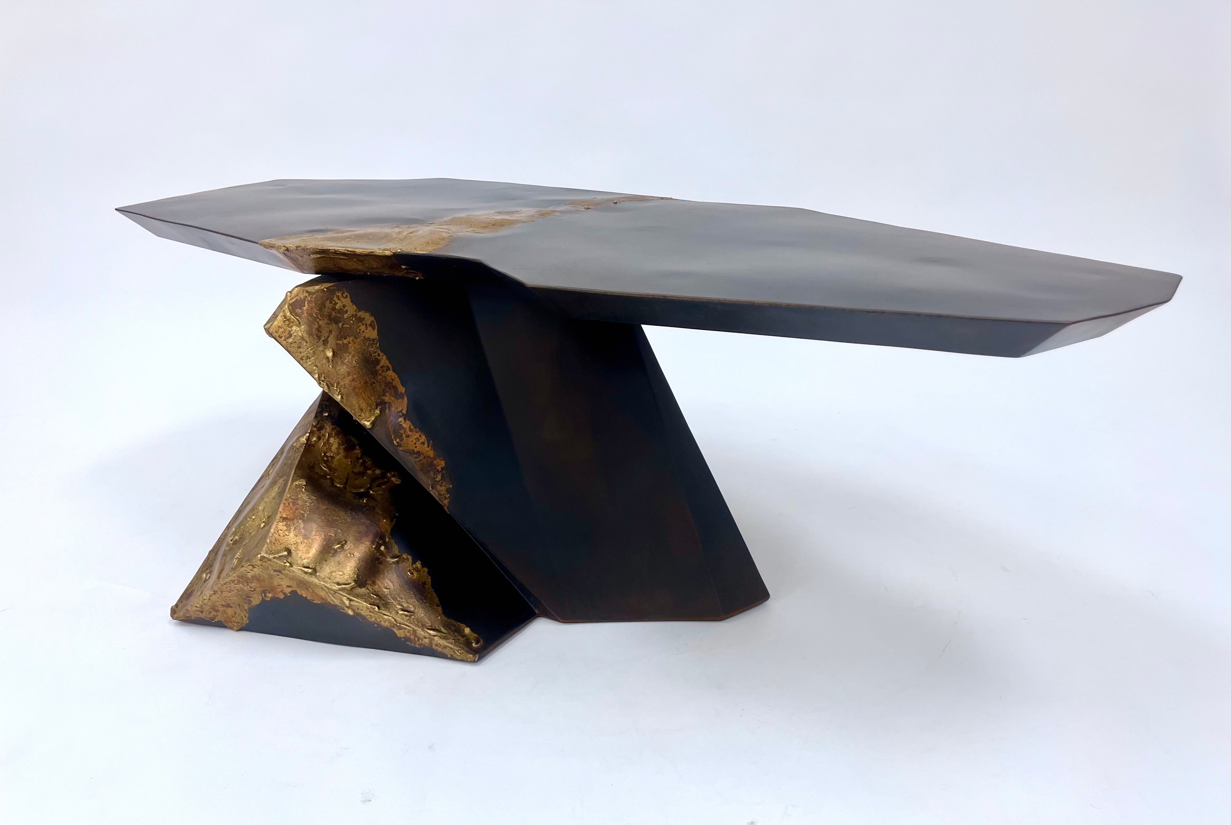 very geometric dark steel base supporting a cantilevered top of dark steel both pieces highlighted by melted bronze that flows through the middle