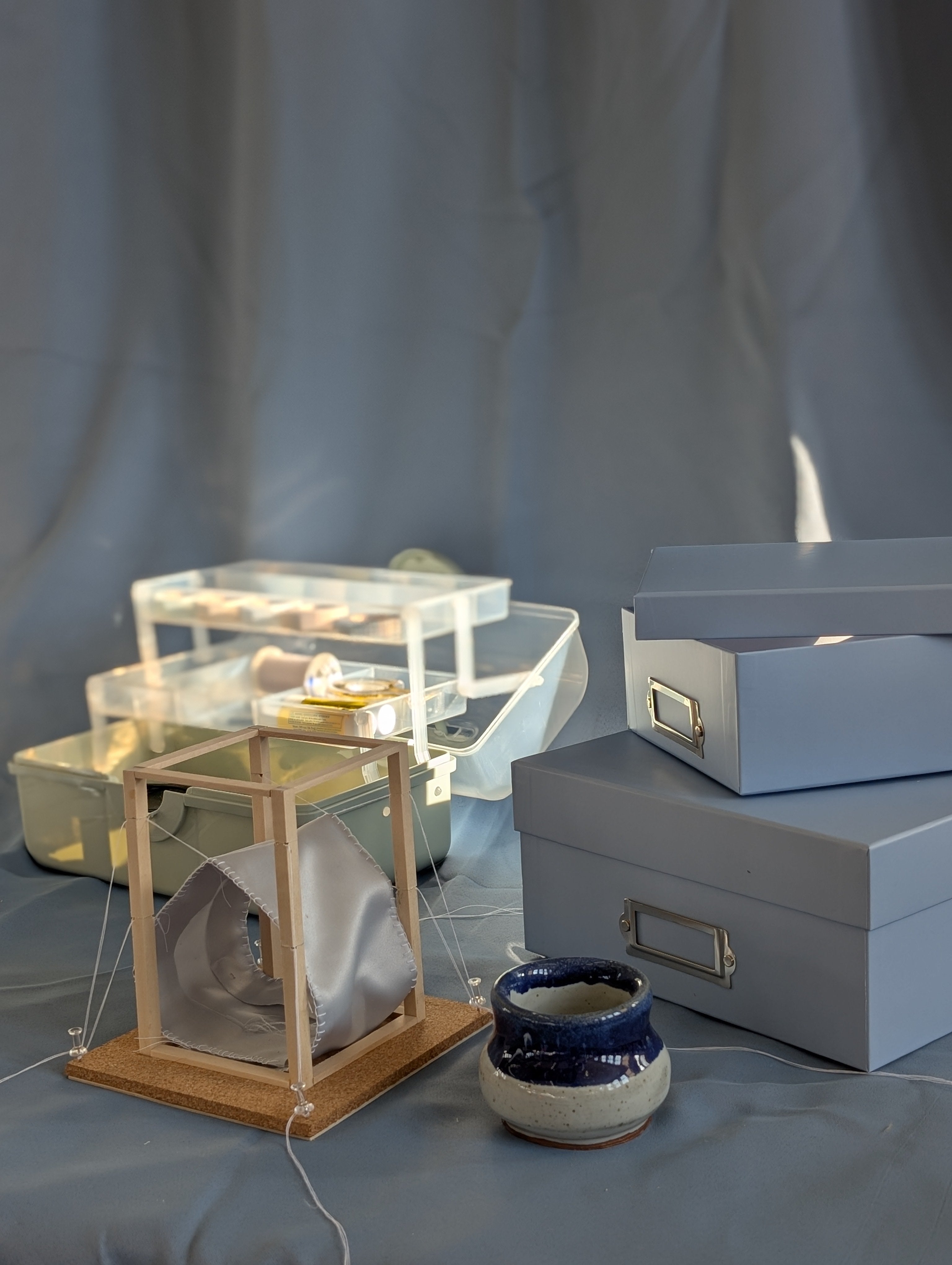 A model with a wooden frame in that supports a pulley system attached to a piece of fabric. The string keeps the fabric in tension creating a house-like shape.