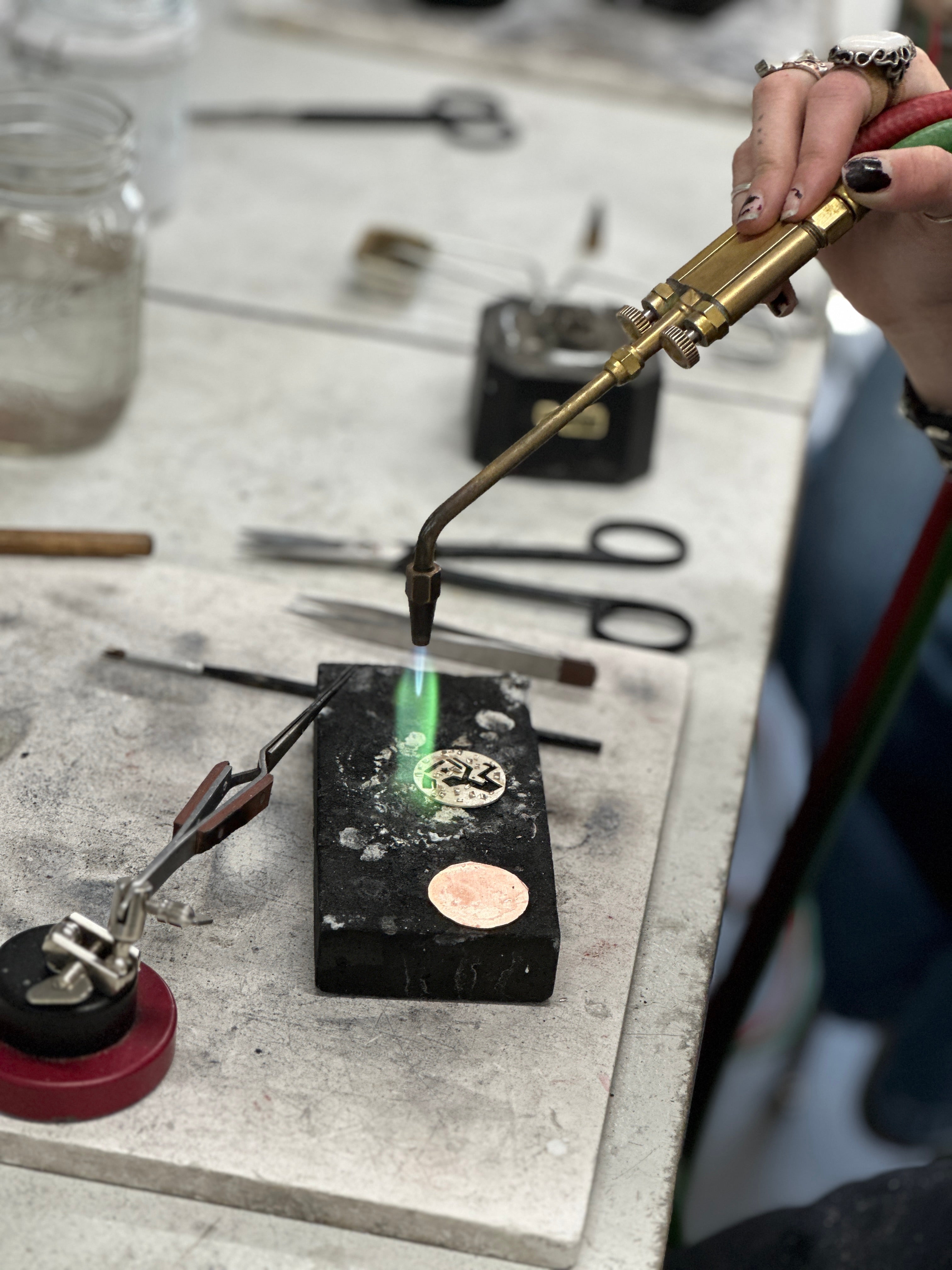 A hand holds a thin torch with a green flame over two copper circles.