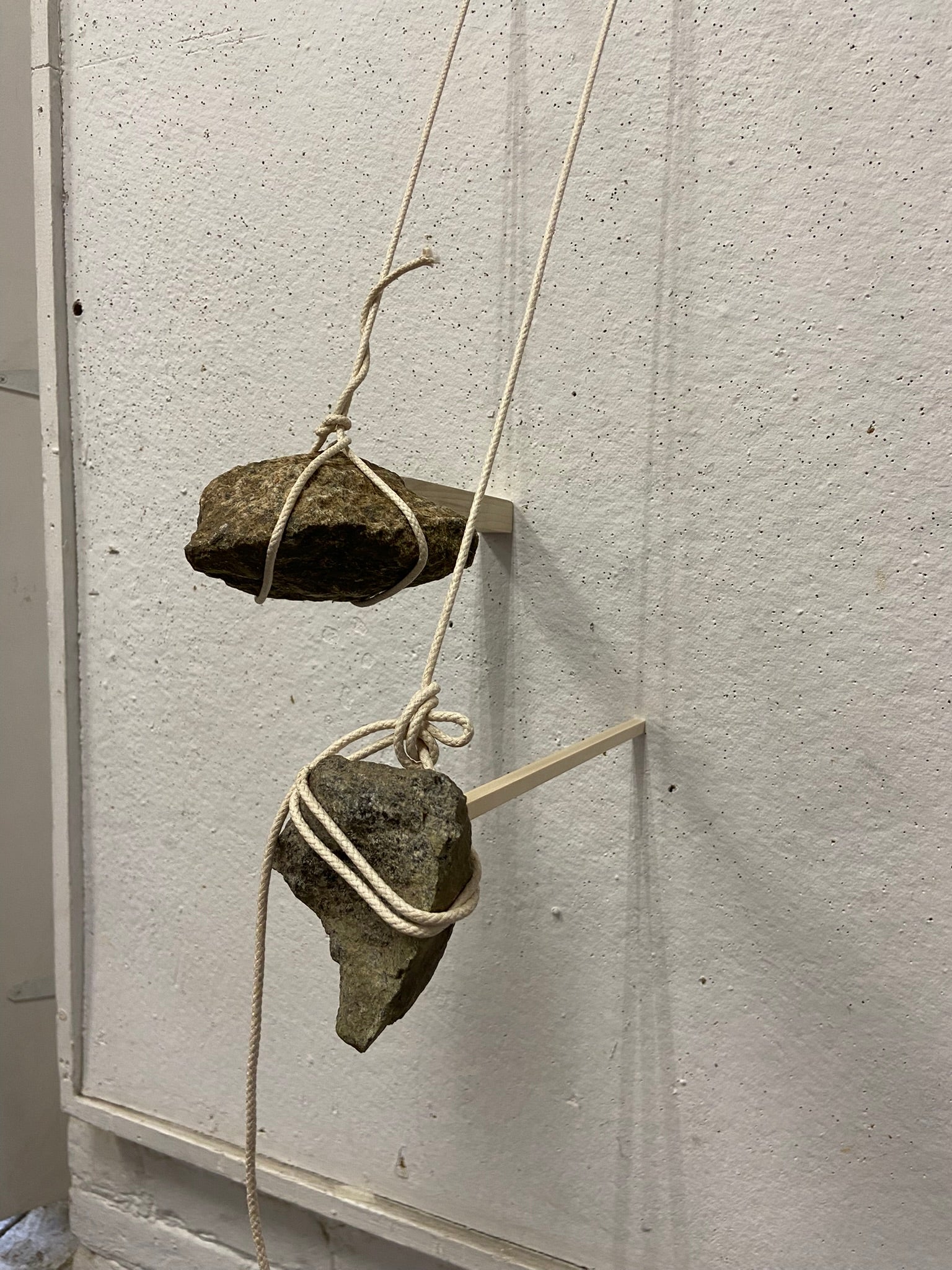 Two rocks hanging from ropes each hold a stick against the wall.