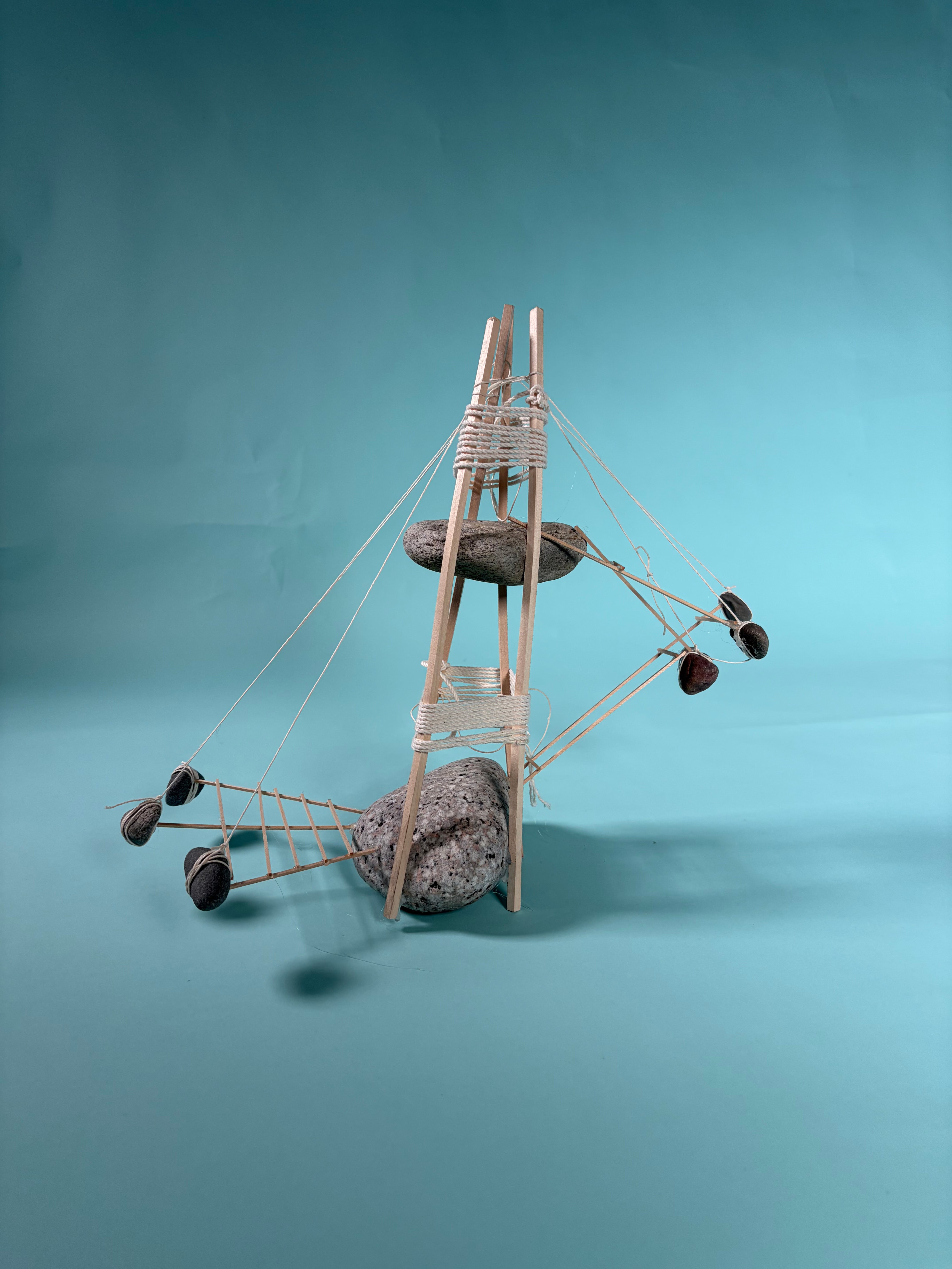 A model made of rock, wood and string. A larger rock on the ground and a smaller rock in the air. Other structures emerge radially, hanging from the top: a deck for research spaces held up by hanging rocks & a set of stairs leading to the top rock platform.