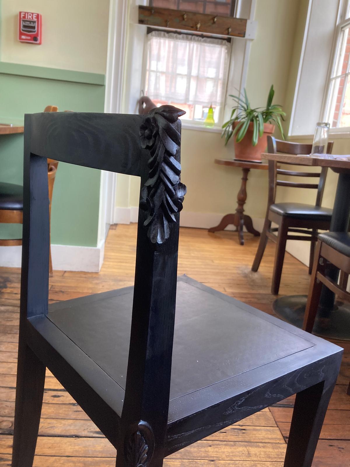 Hand-carved wood chair leg detail featuring subtle leaf motif, demonstrating traditional chisel work applied to modern dining furniture