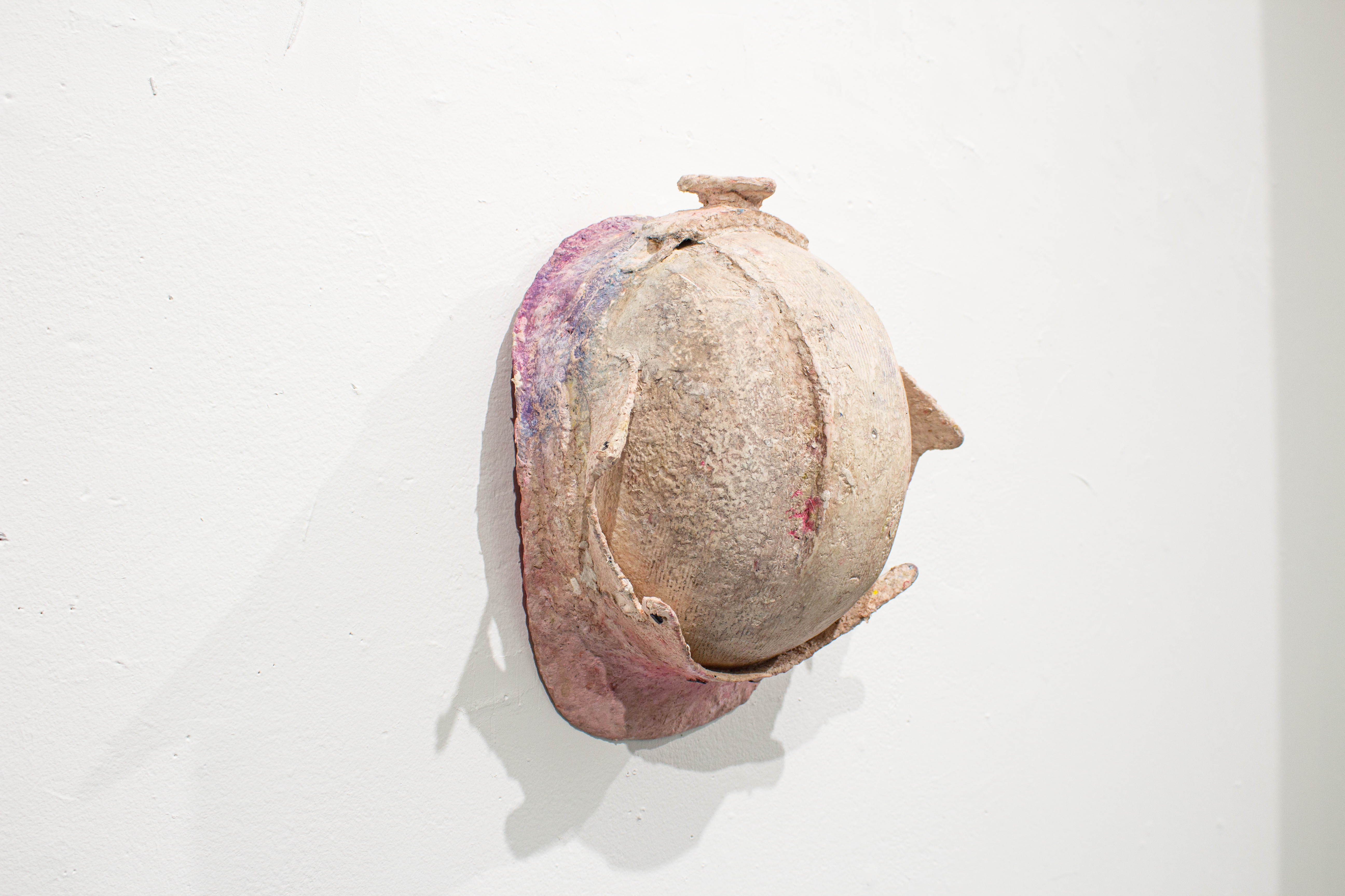 A construction worker's helmet covered by a crusty pink material. Hung flat on the wall.