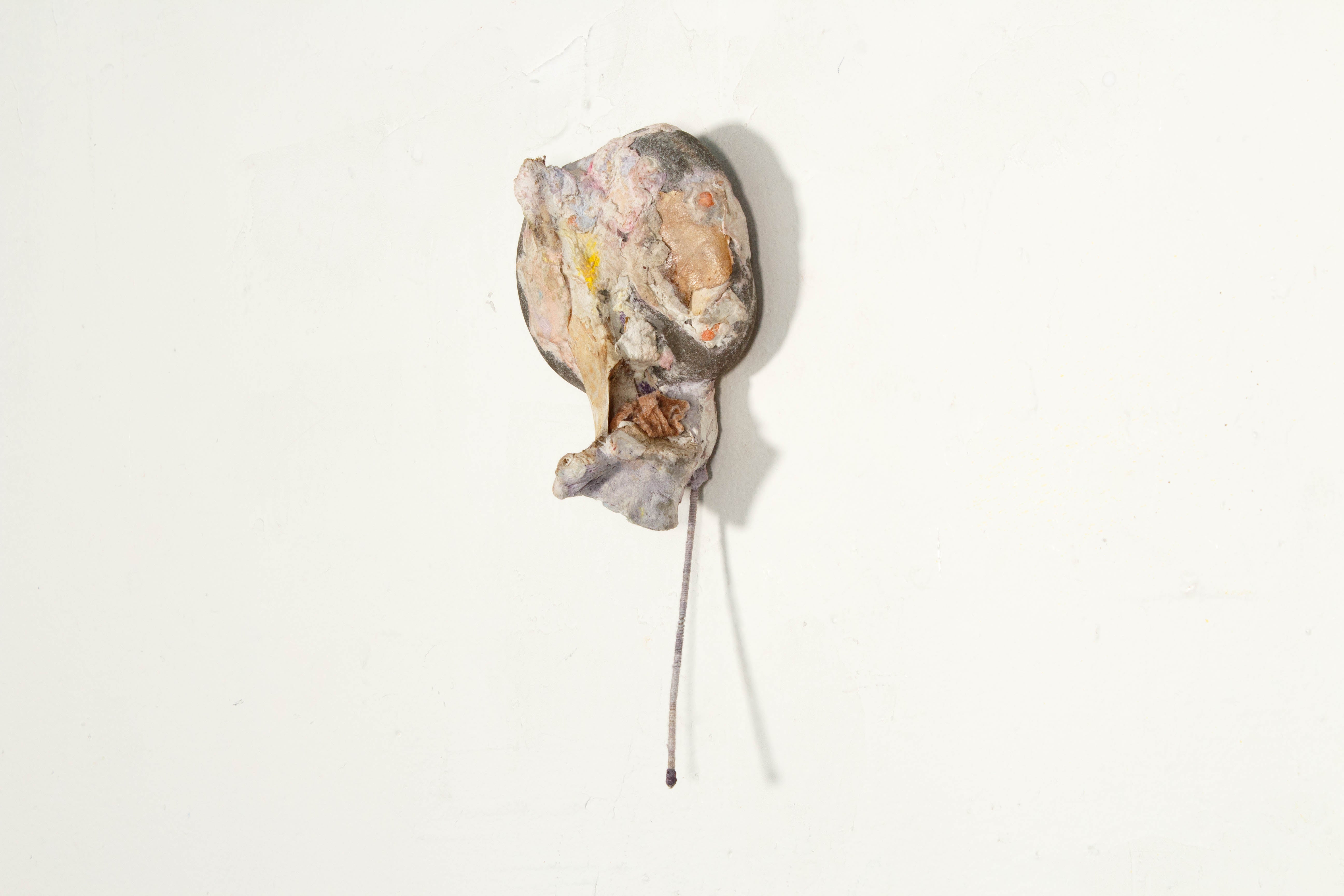 A hanging wall sculpture made with a rock covered by paper mache with a thin metal stem.