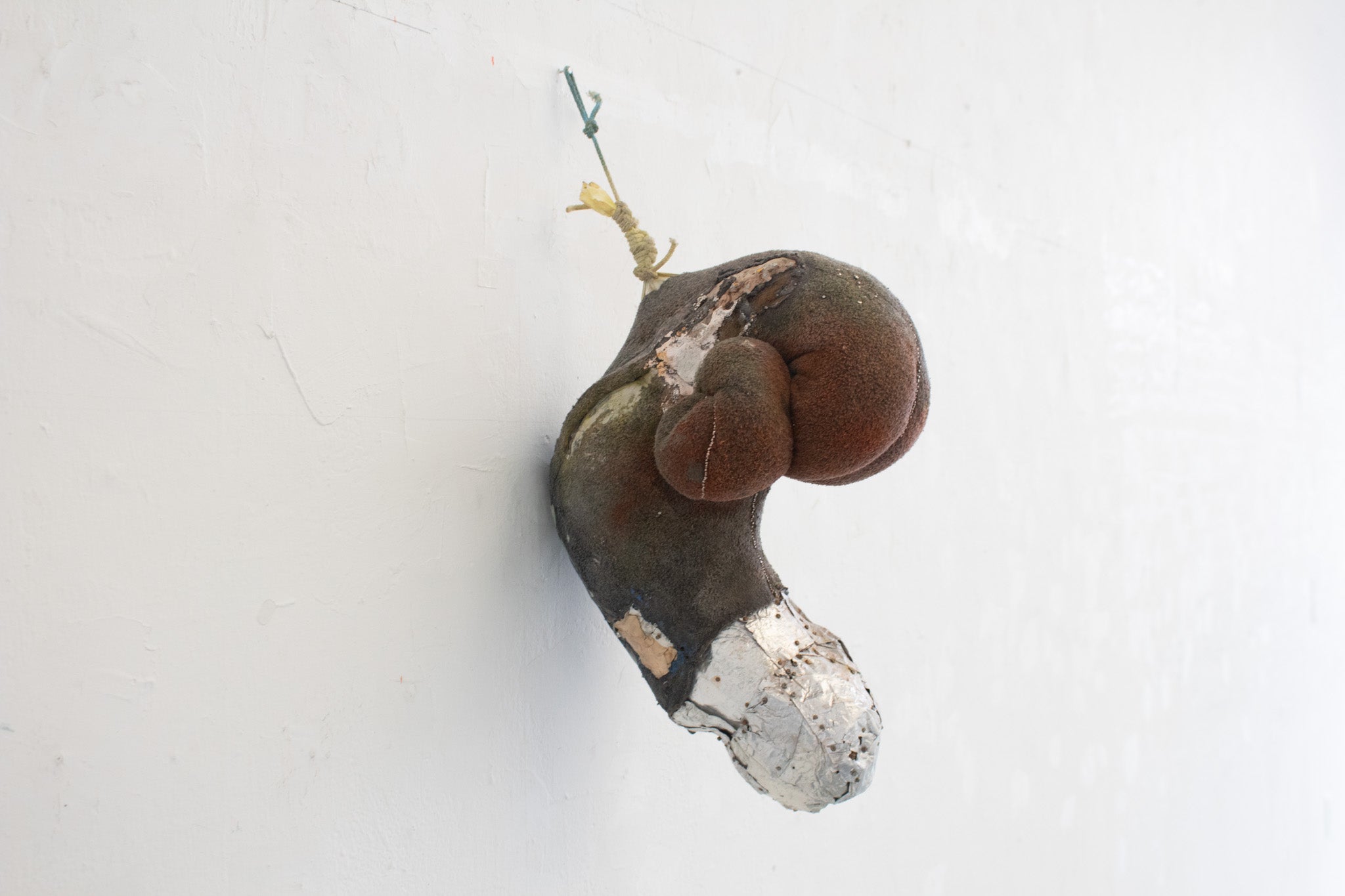 a twisted green neck pillow stiffened with glue. Its end is covered by squares of aluminum and nails, there are pins running along its seams.