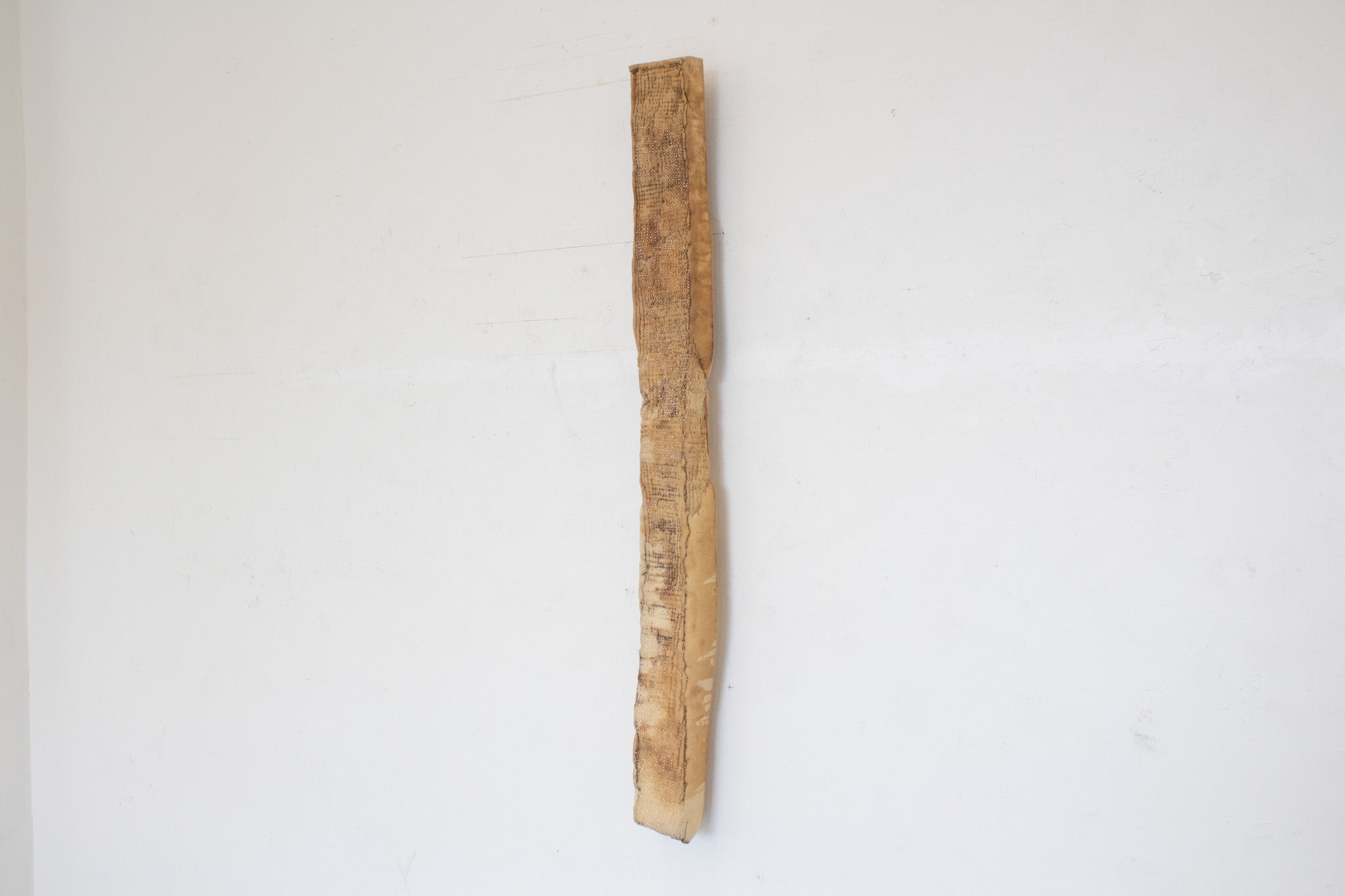a long piece of foam covered in a grid of glimmering pins. Red ribbon necklace tied around the top of the piece hangs it from the wall so that it barely touches the floor.