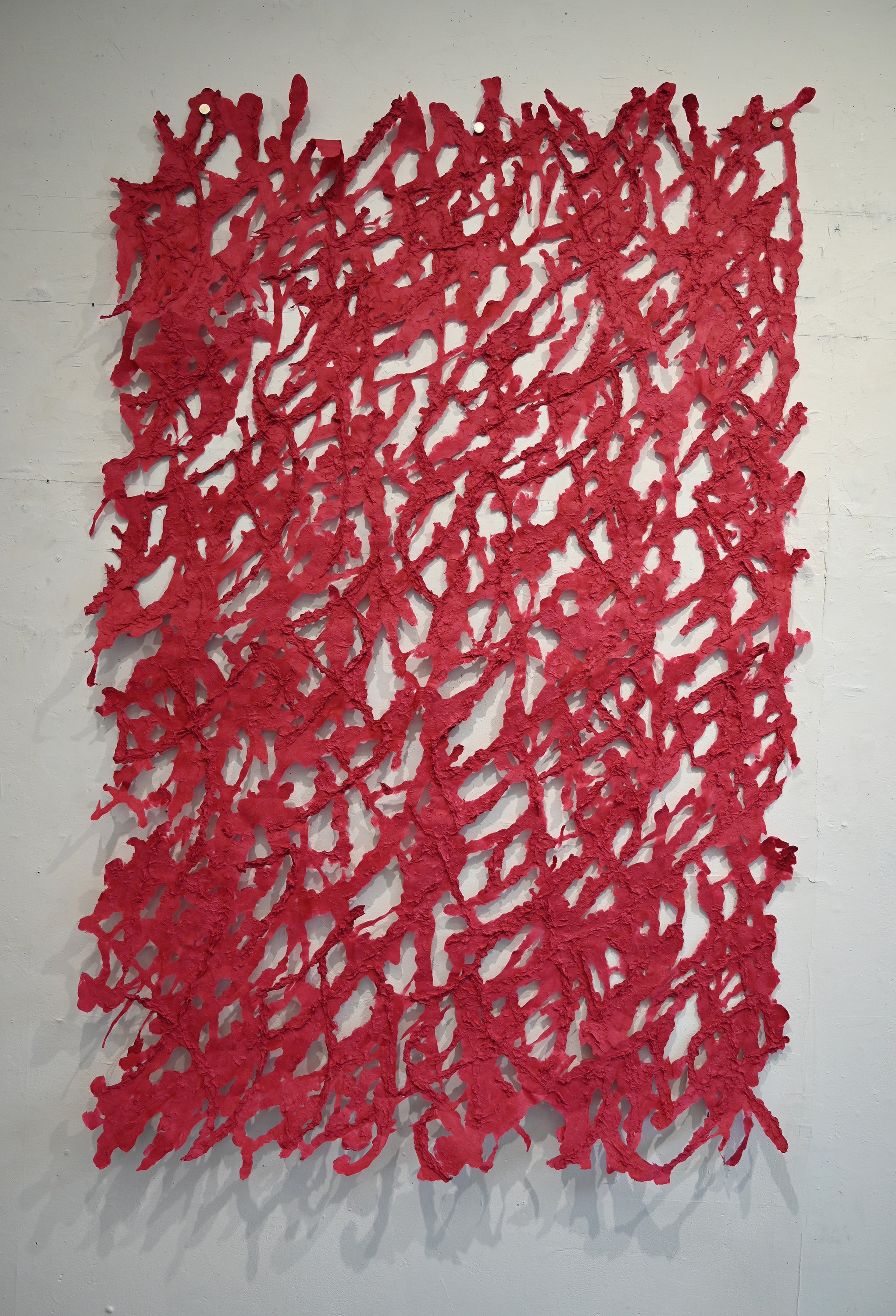 Web-like shape red pulp painting hanging on a white gallery wall