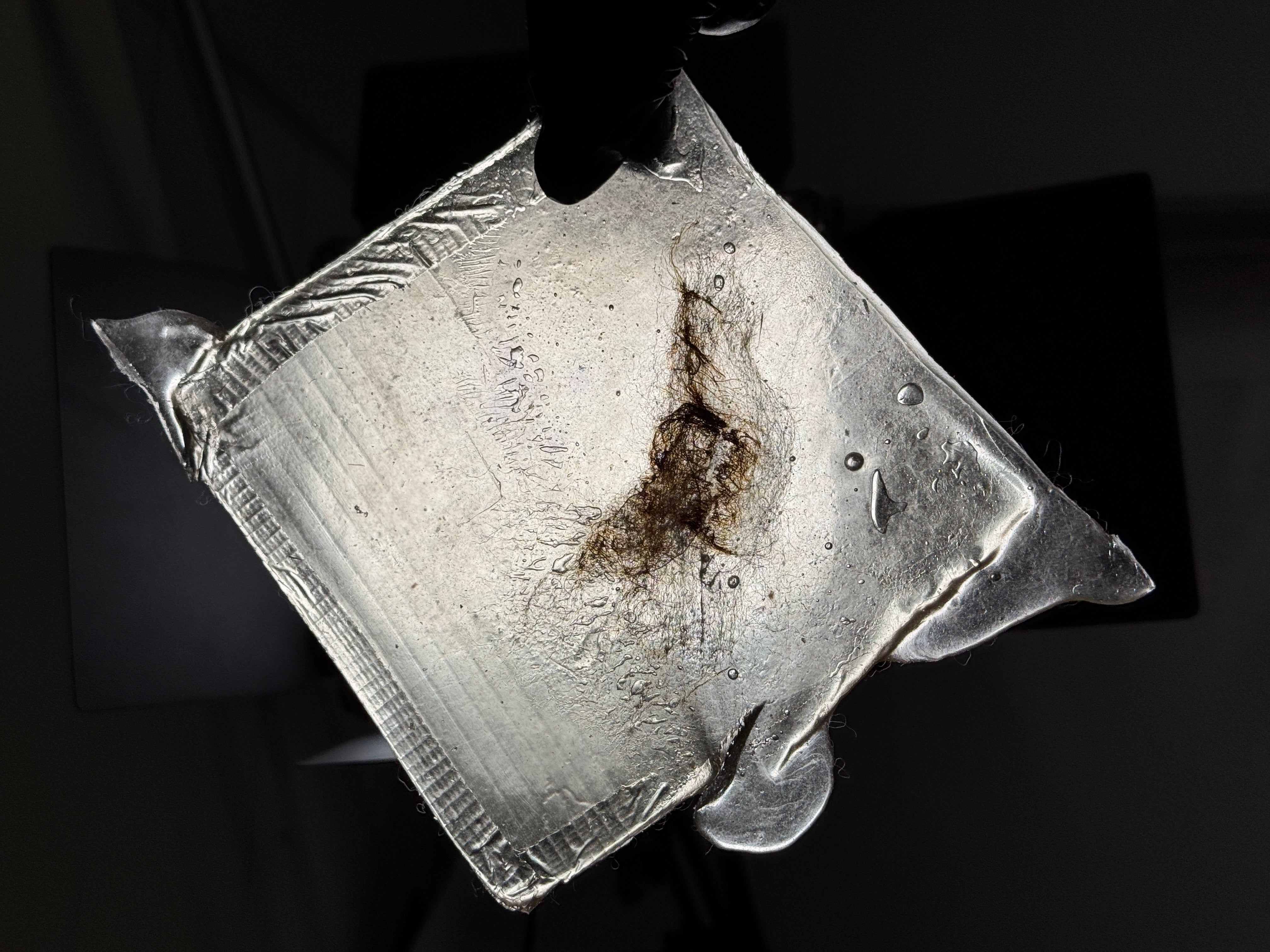 A bioplastic sheet made from a blend of wool and gelatin. 6 inches by 6 inches. The torn gelatin is heated until melted and then reformed. The charred wool reveals a distinct texture.