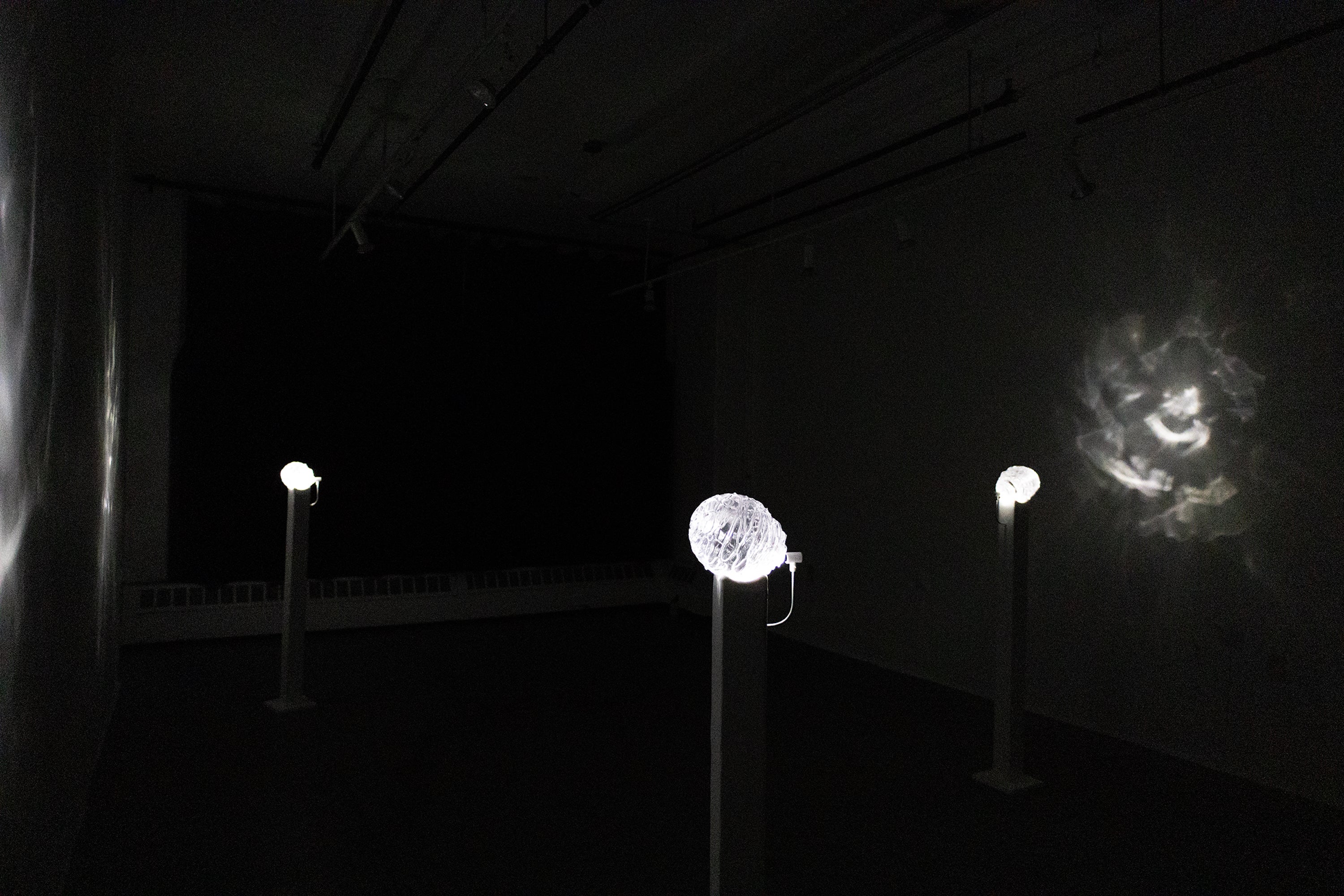 A dark room with three glass orbs on tall, thin pedestals. A small light shines on each orb, causing the orbs to glow and cast caustic light effects onto the walls nearby. 