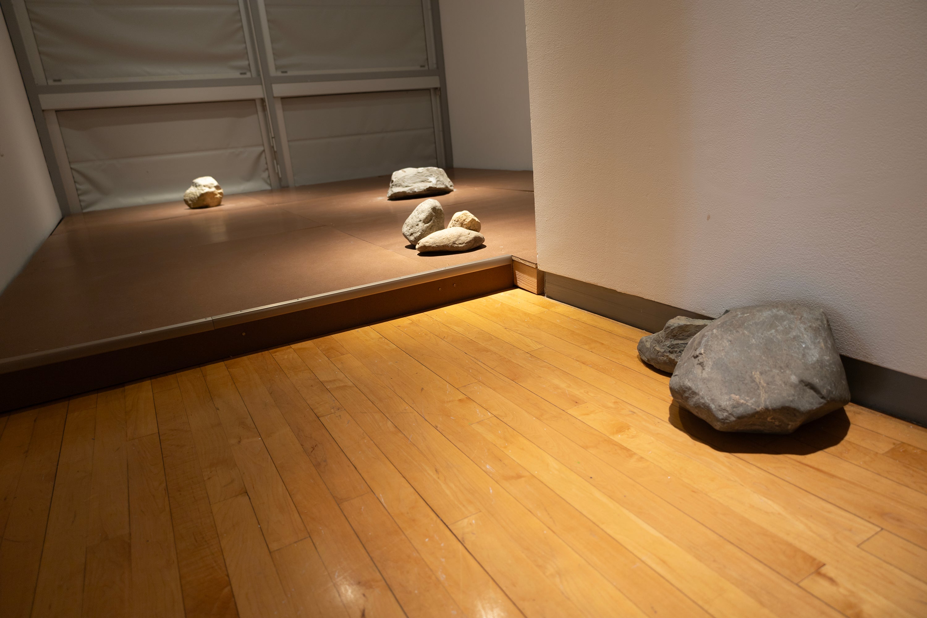 A brown, raised flooring with 4 groupings of large rocks. The rocks are lit from above, highlighting their presence on the flooring. 
