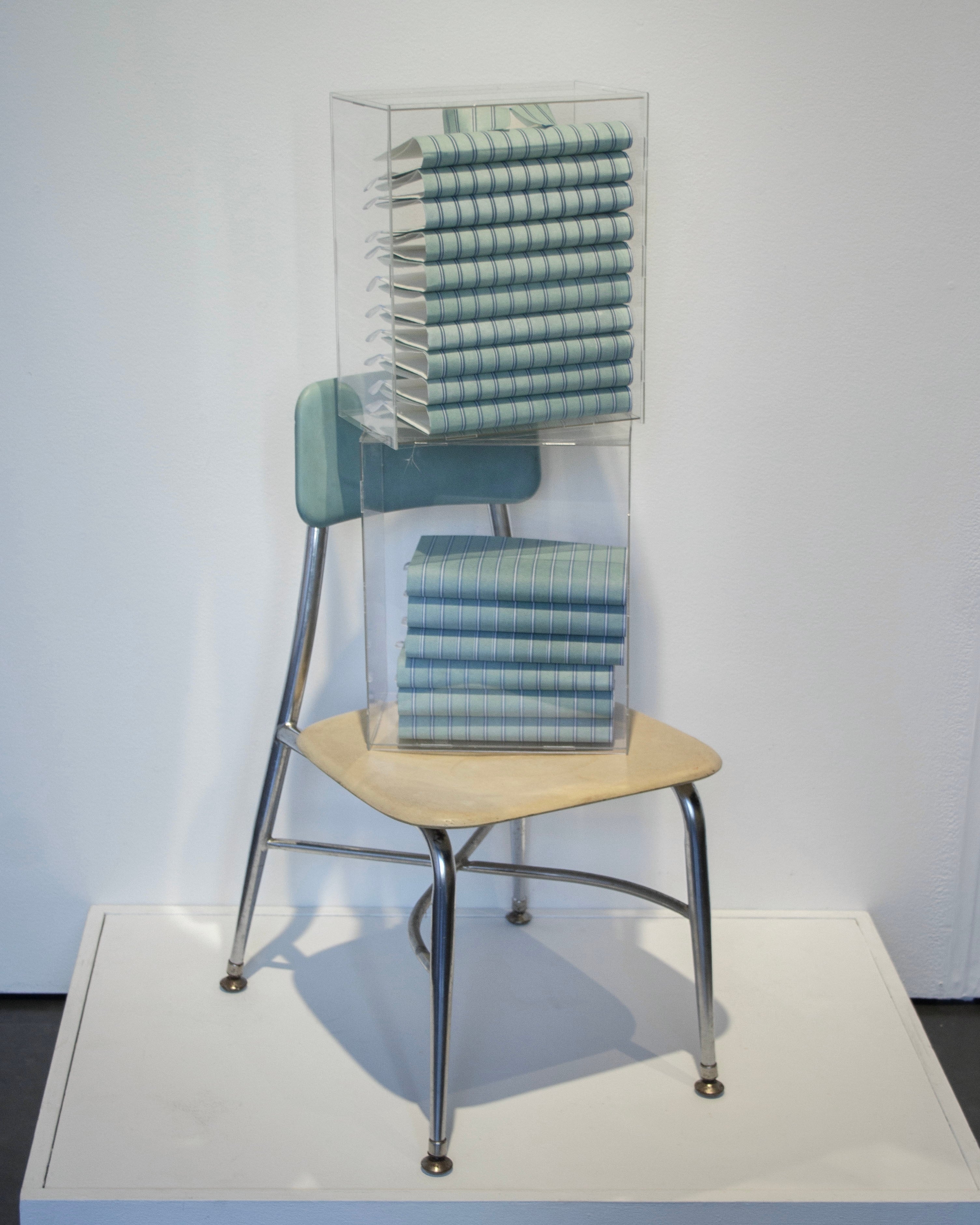 Three-layer photopolymer letterpress on kozo paper, folded and stacked in acrylic boxes to mimic folded shirts, placed on top of a found wooden chair.