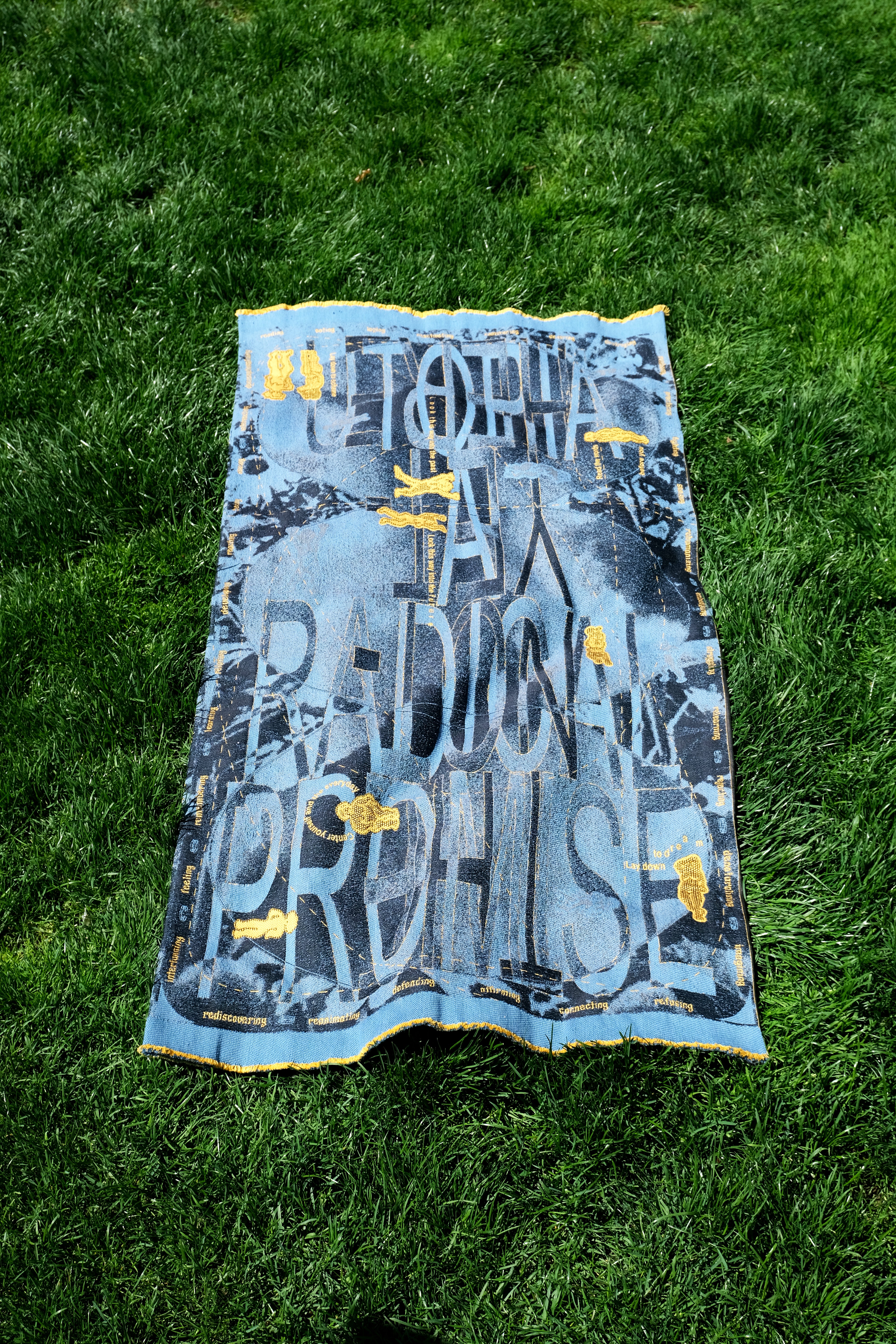 A blue and yellow-gold typographic textile on grass