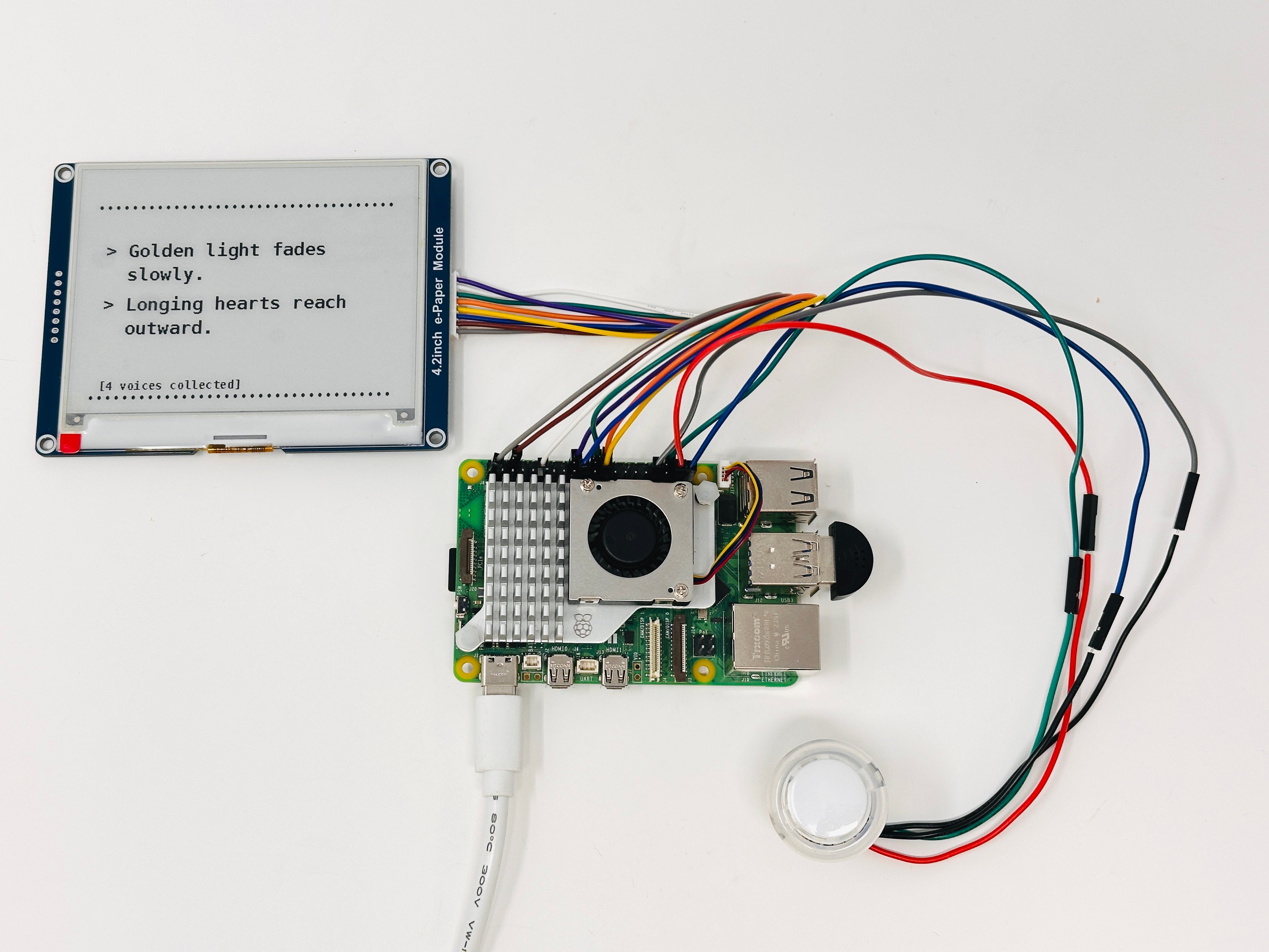 Electronics for the Spark installation, including a Raspberry Pi, e-paper display, button, and wiring. The display shows generated poetic summaries and the number of collected voice submissions from a specific location.