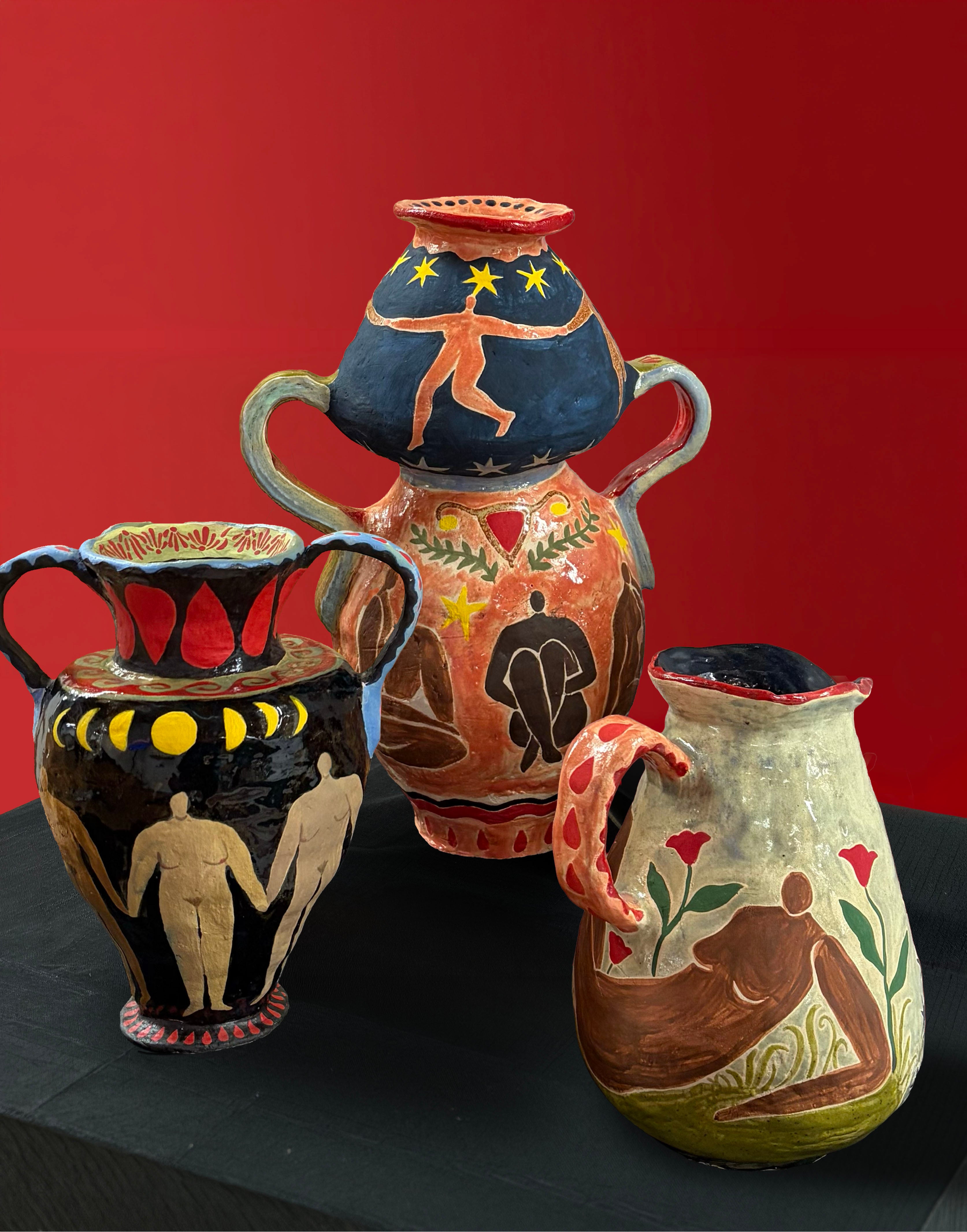 Three hand-painted ceramic vessels featuring figures, moons, stars, flowers, and menstrual imagery displayed on a black pedestal against a deep red background.
