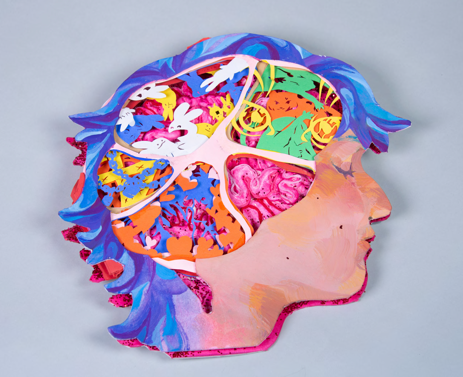 Tunnel book made with, museum board, paper, gouache, acrylic, air dry clay, glitter, glue and gloss finish. Book shaped of a face side profile, where the brain should be is an opening with 5 sections. 1 of a brain, one of bunny like creatures, one with memories locked away and one of love. 