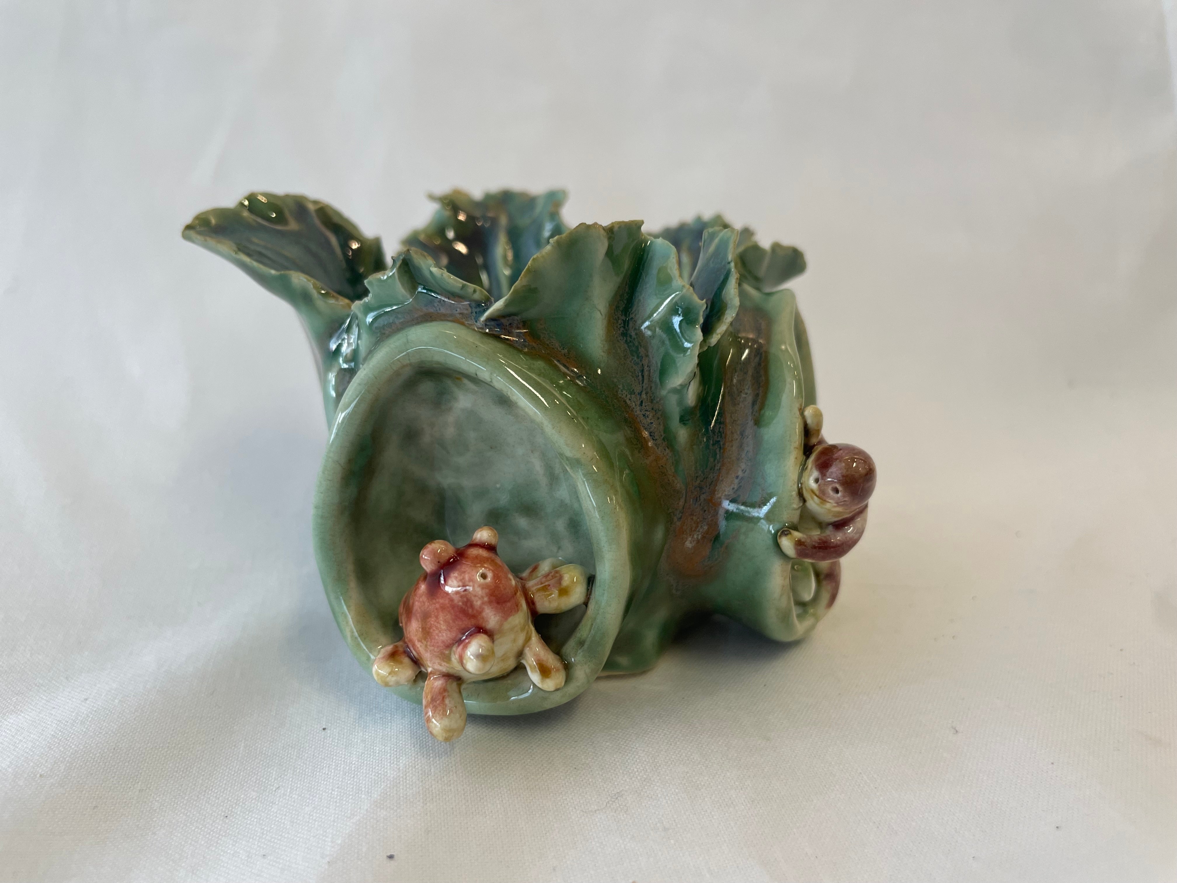 Ceramic bowel made using pinching clay techniques to have a lettuce like appearance, two hand sculpted creatures are on the outside in their own built in holes on the outside of the bowl. Both creatures are peaking around the corner to say hi to each other. Creatures are glazed orange and brown, lettuce bowl is green.